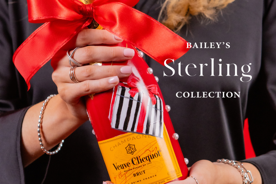 Person holding a bottle of Veuve Clicquot with a red ribbon, featuring Bailey's Sterling Collection branding.