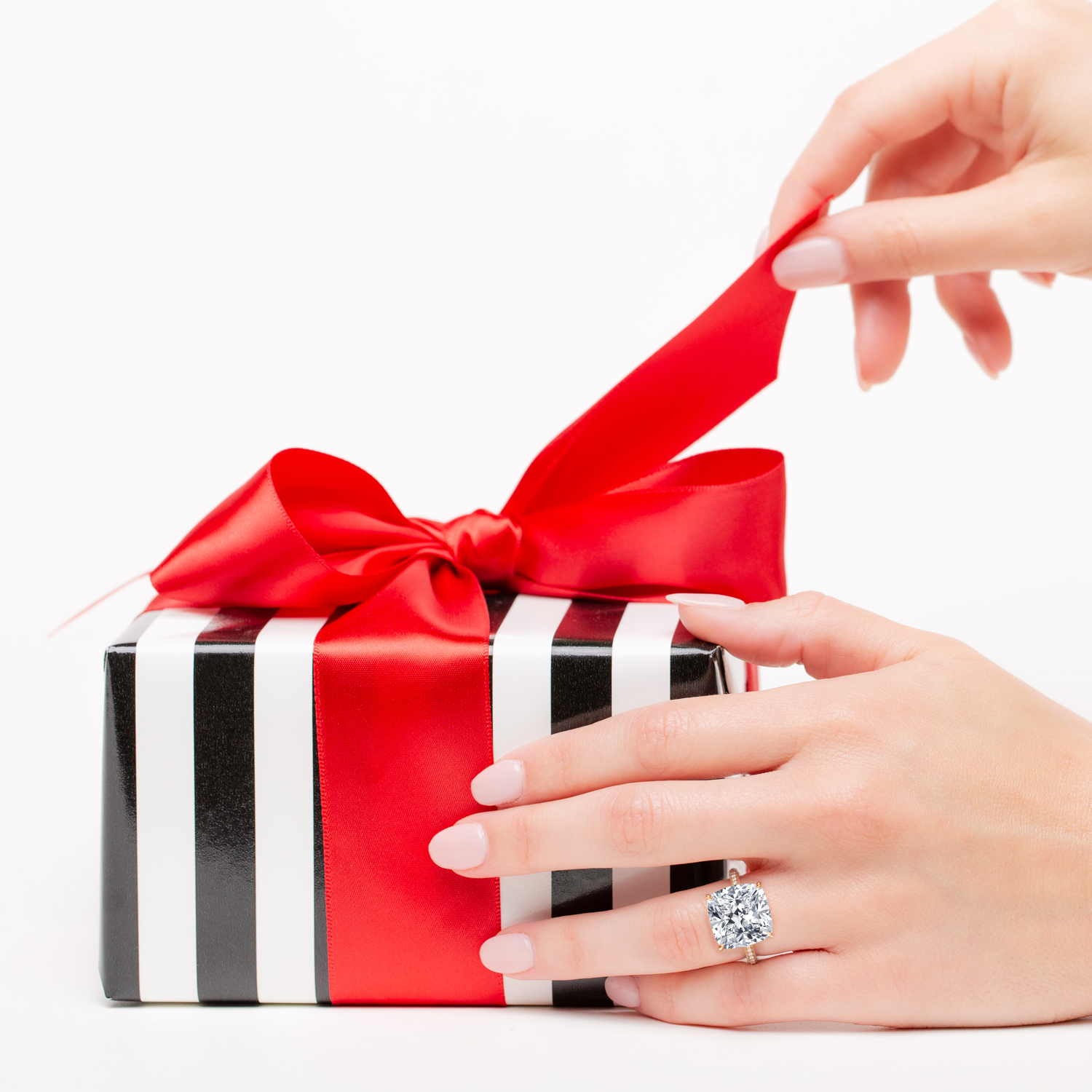 Hand with a diamond ring holding a gift box with a red ribbon on a white background