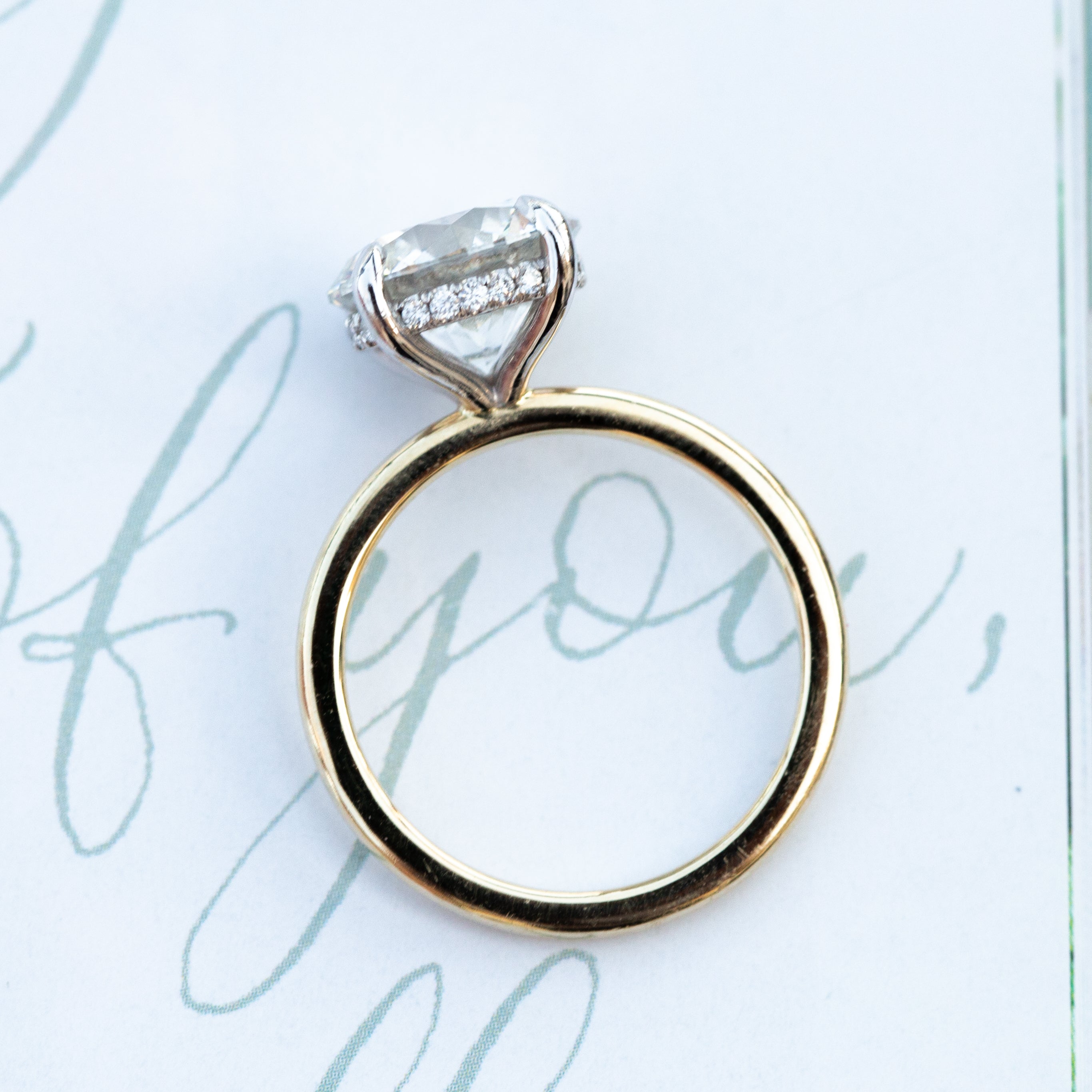 Gold ring with a diamond on a light blue background with cursive text