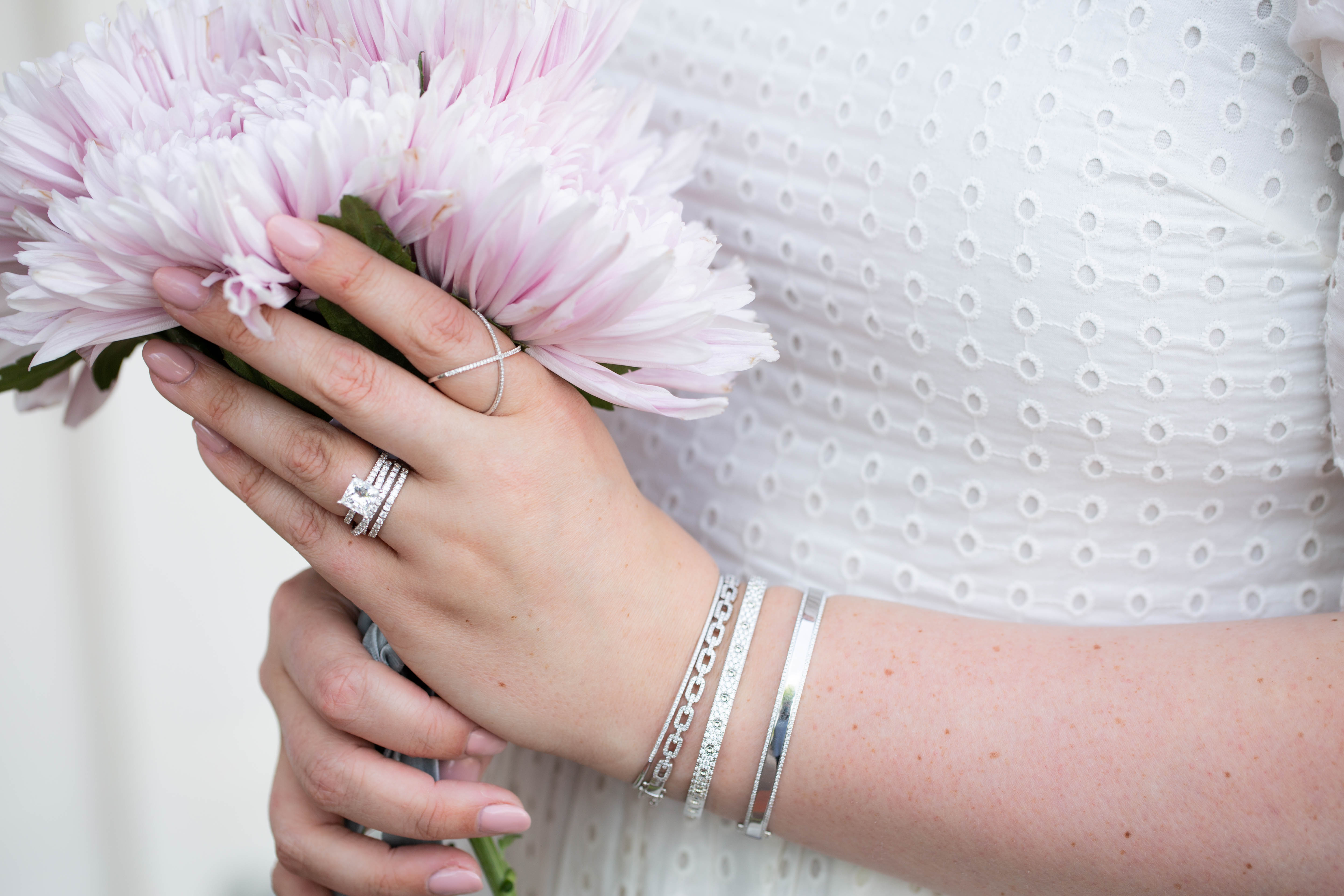 Hand holding pink flowers with silver rings and bracelets on a blurred background