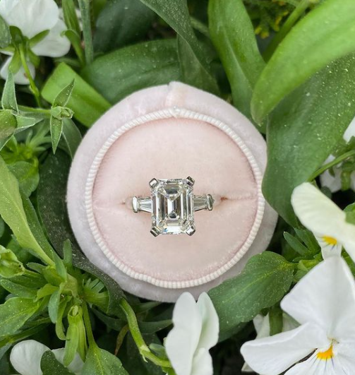 diamond ring in a circular pink box with green leaves and white flowers in the background