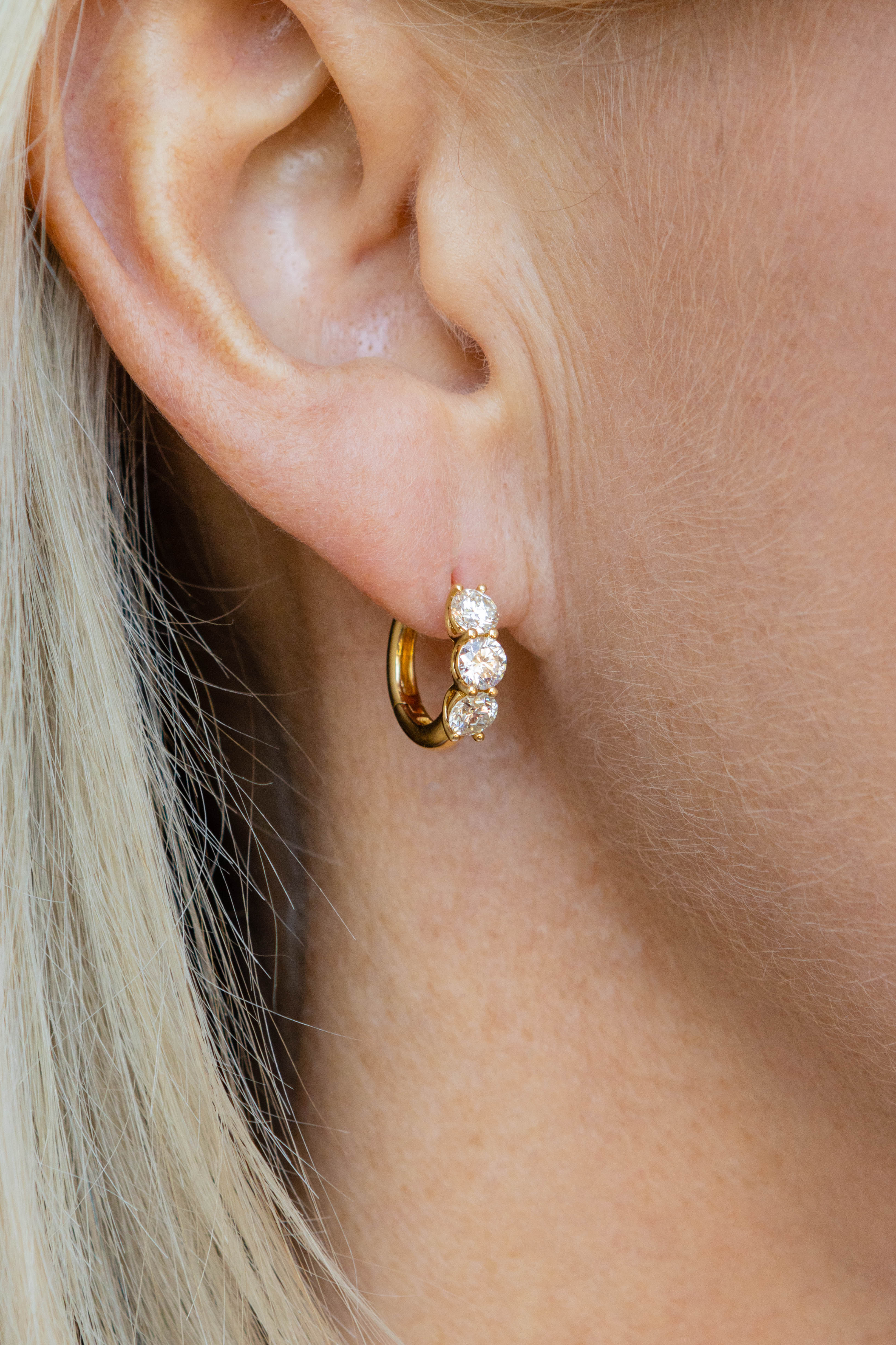 Close-up of an ear wearing a gold hoop earring with clear gemstones.