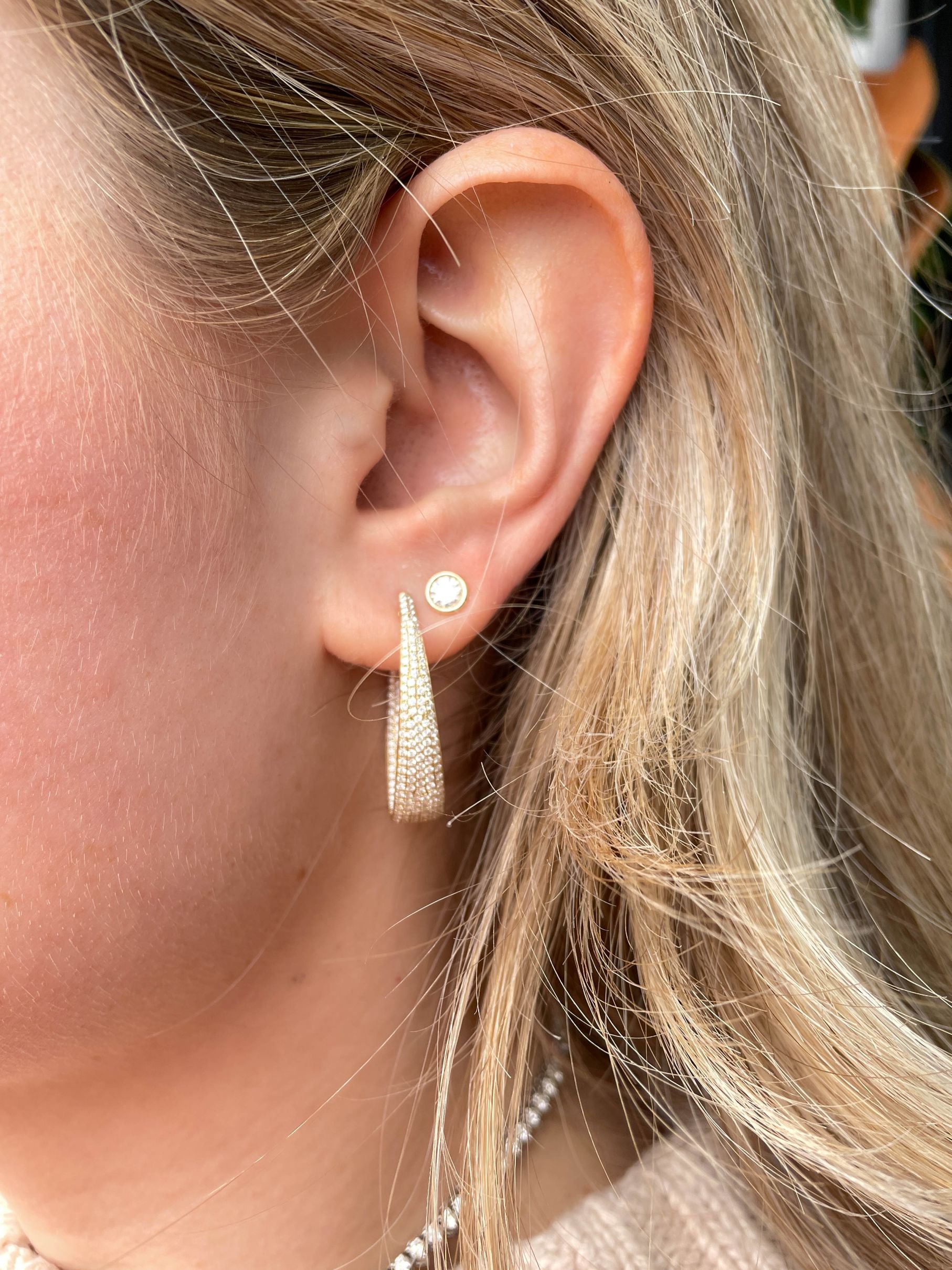 Close-up of an ear wearing a gold earring with a blurred background
