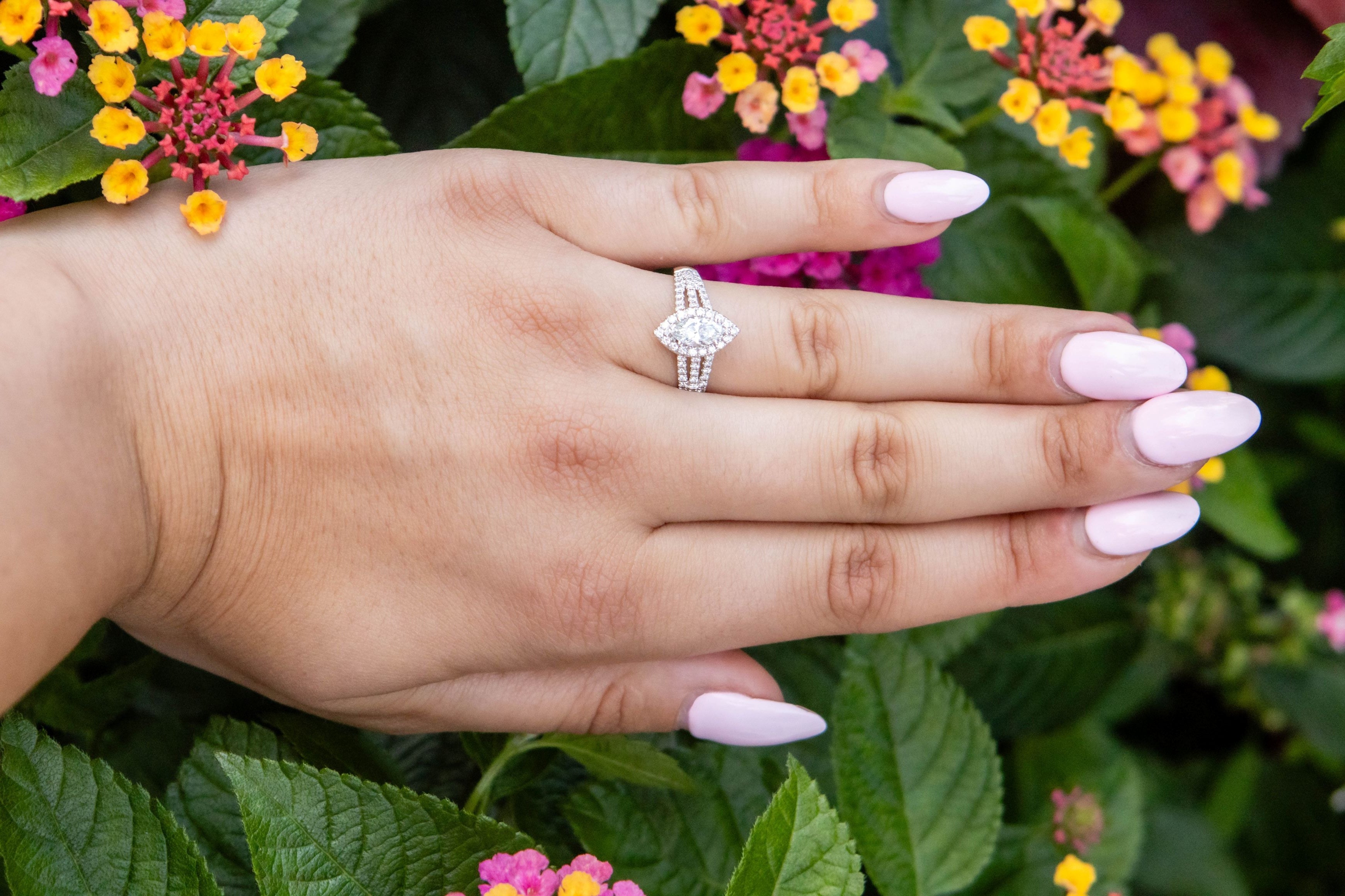 Hand with a silver diamond ring on a background of colorful flowers and green leaves
