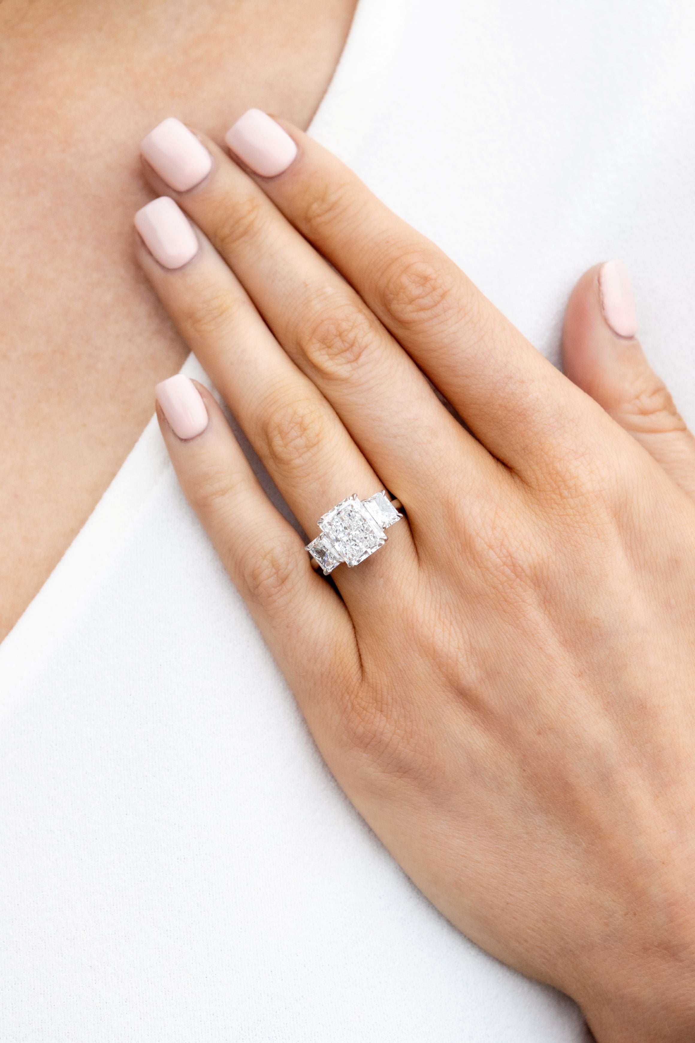 hand wearing diamond ring on a white and neutral background