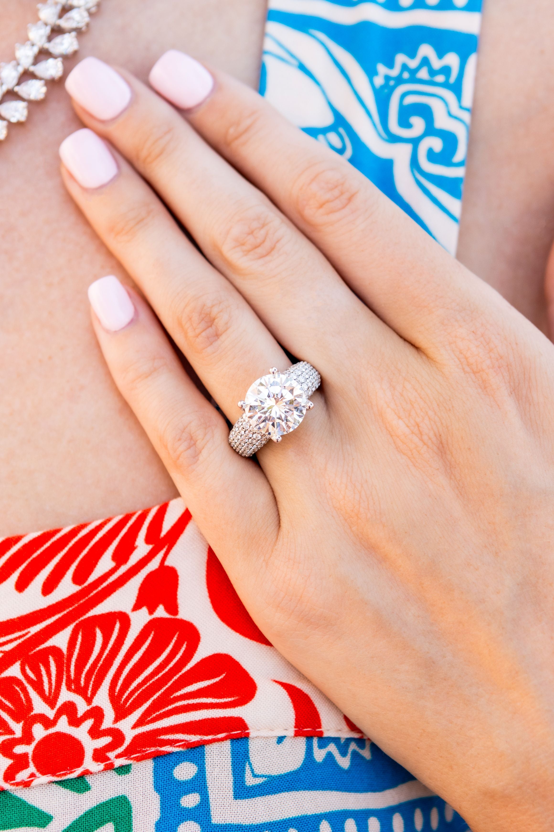 Close-up of a hand wearing a diamond ring with a colorful fabric background