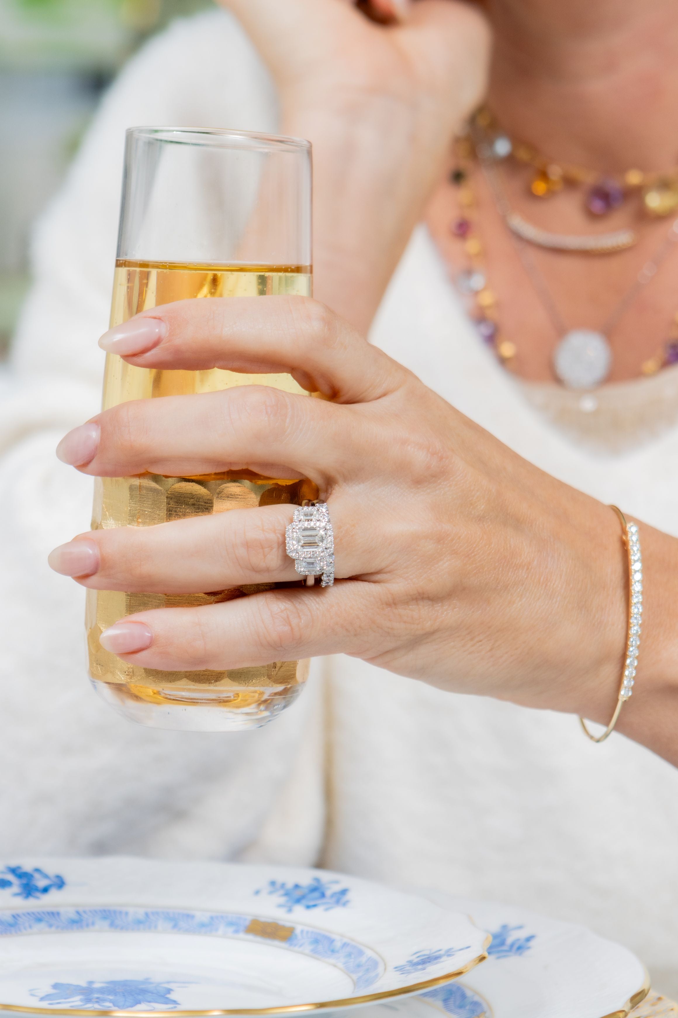 Hand holding a glass of champagne with a diamond ring on a white plate