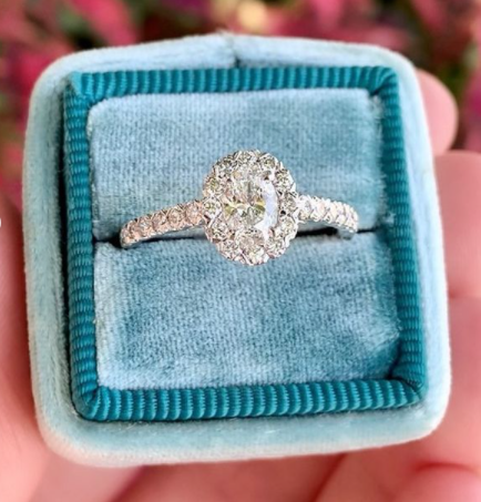oval diamond ring in blue fabric box with blurred pink background