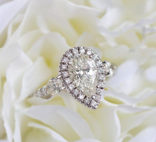 Diamond ring with a pear-shaped center stone on a white floral background