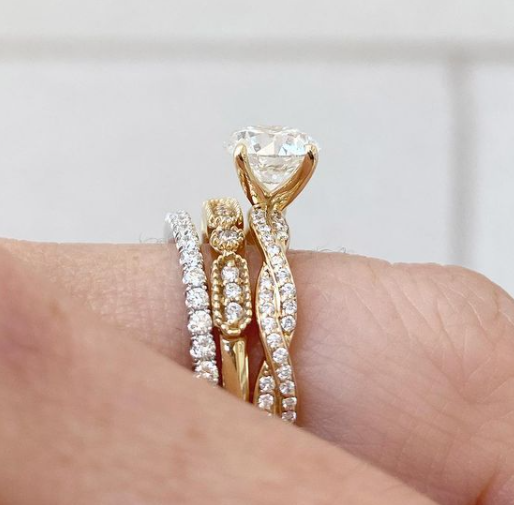 Gold and diamond rings on a finger against a neutral background