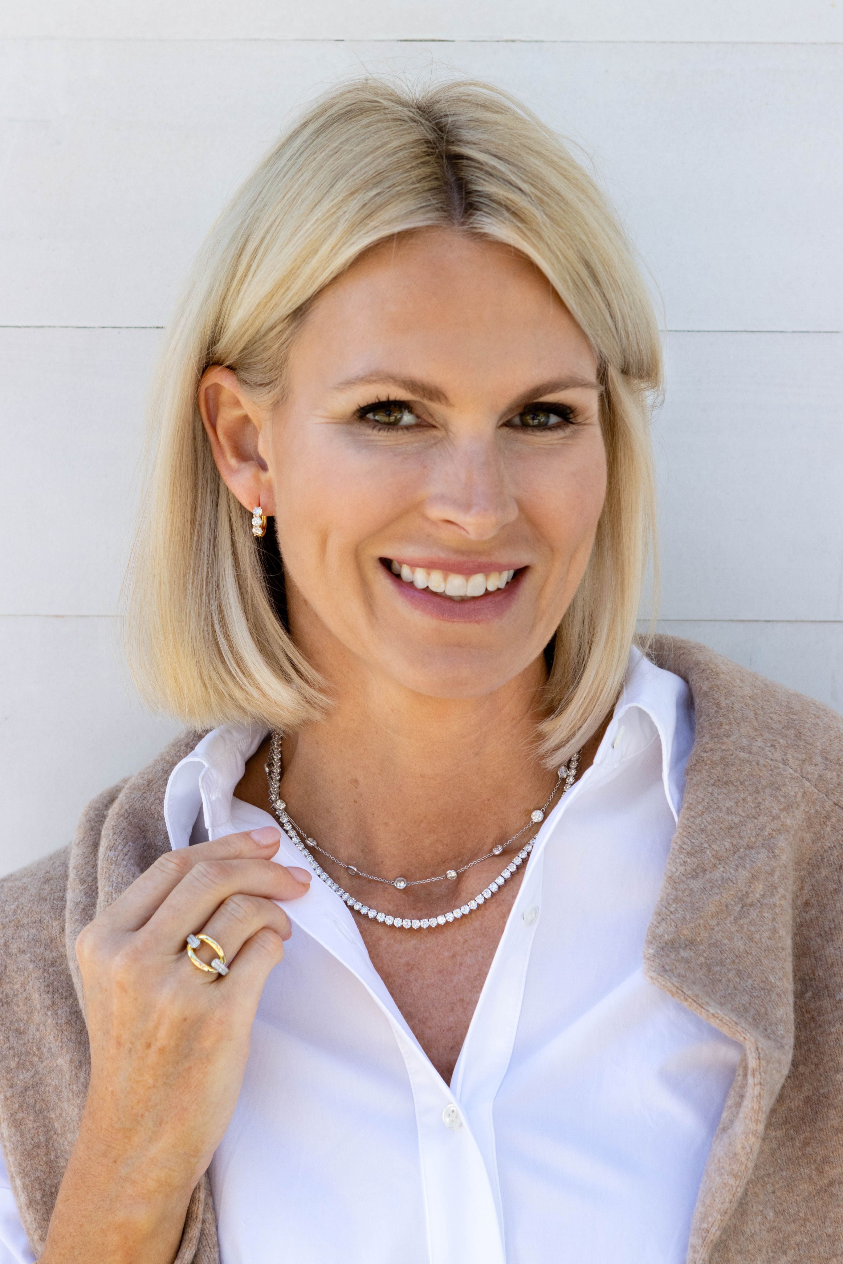Woman with blonde hair wearing a white shirt and beige cardigan against a light background