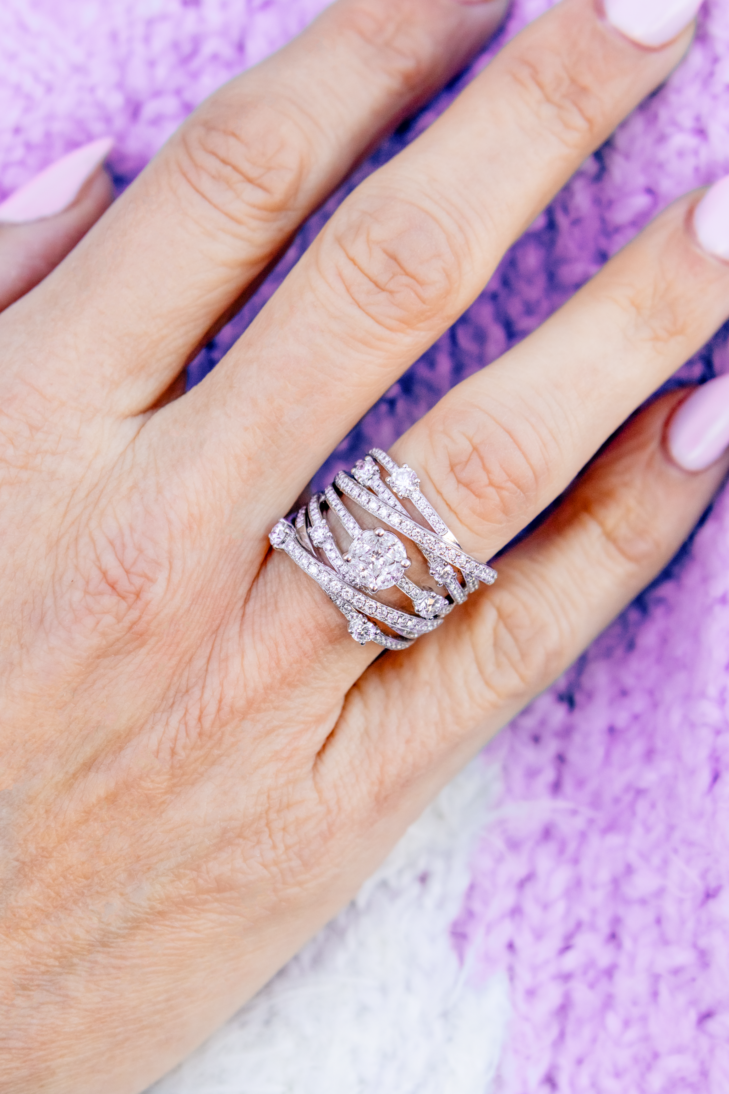 Hand wearing a stack of diamond rings on a purple textured background