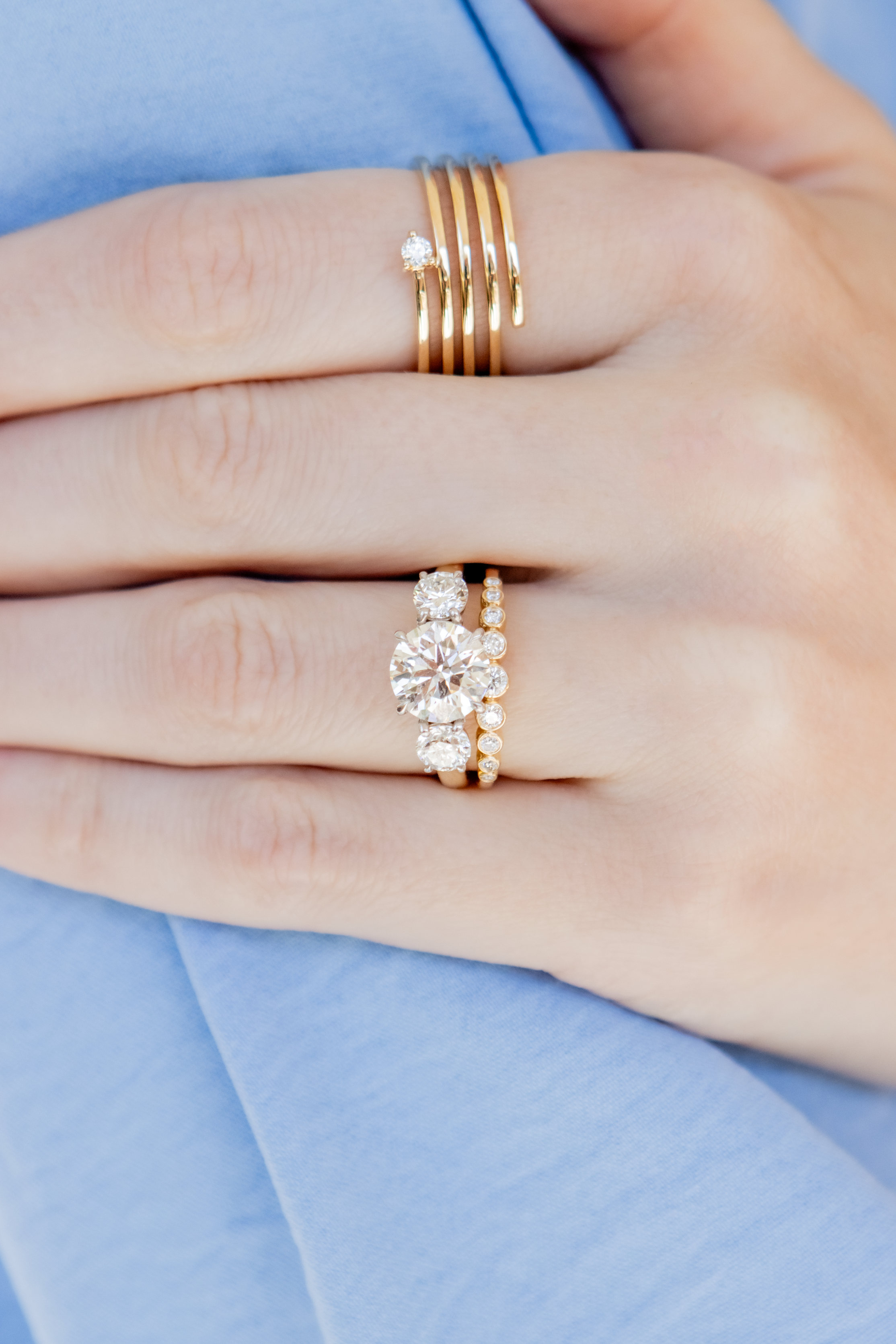 Close-up of a hand wearing three gold diamond rings on a light blue fabric background