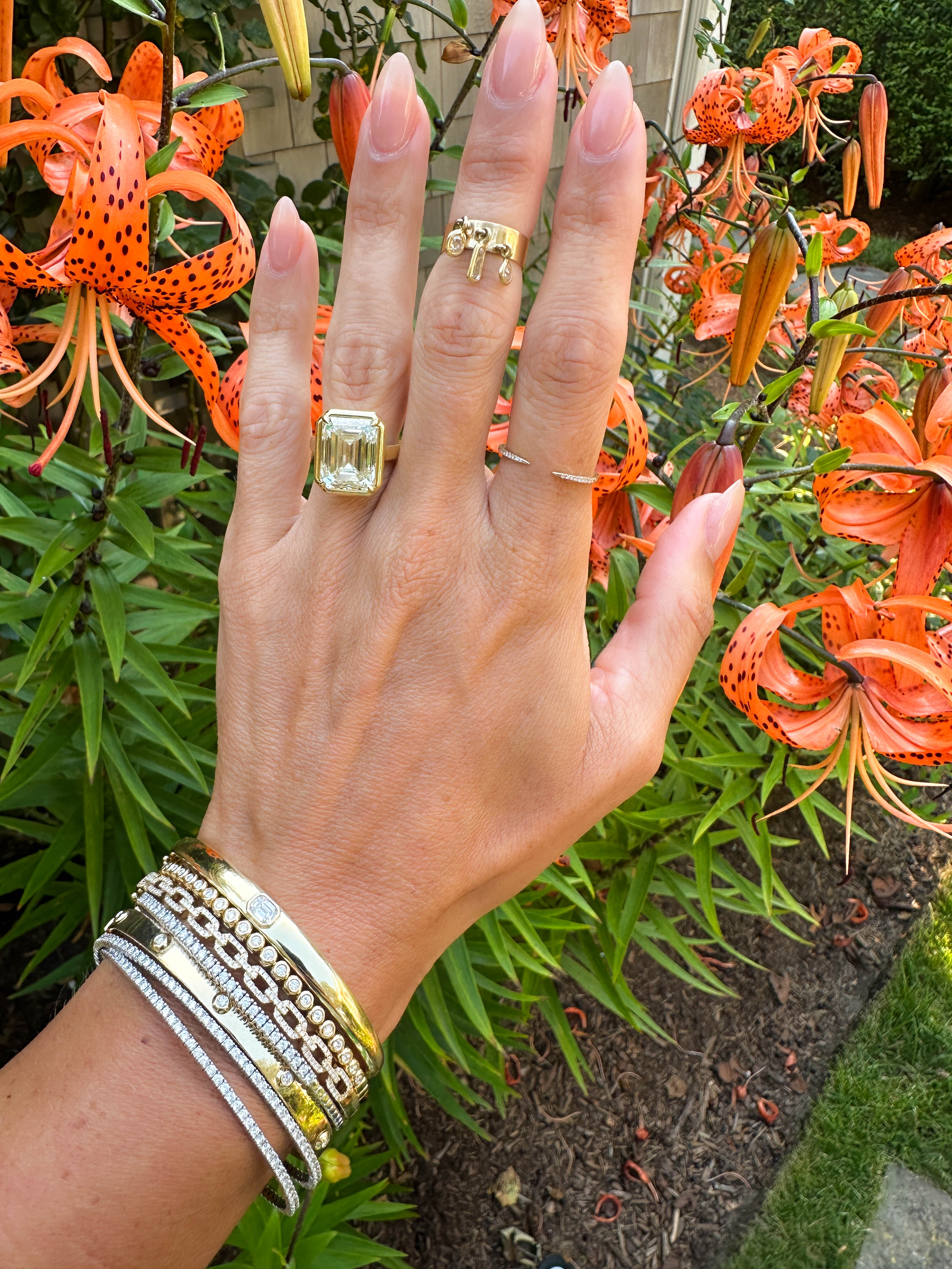 Hand wearing a gold ring with a yellow gemstone against a background of orange lilies.