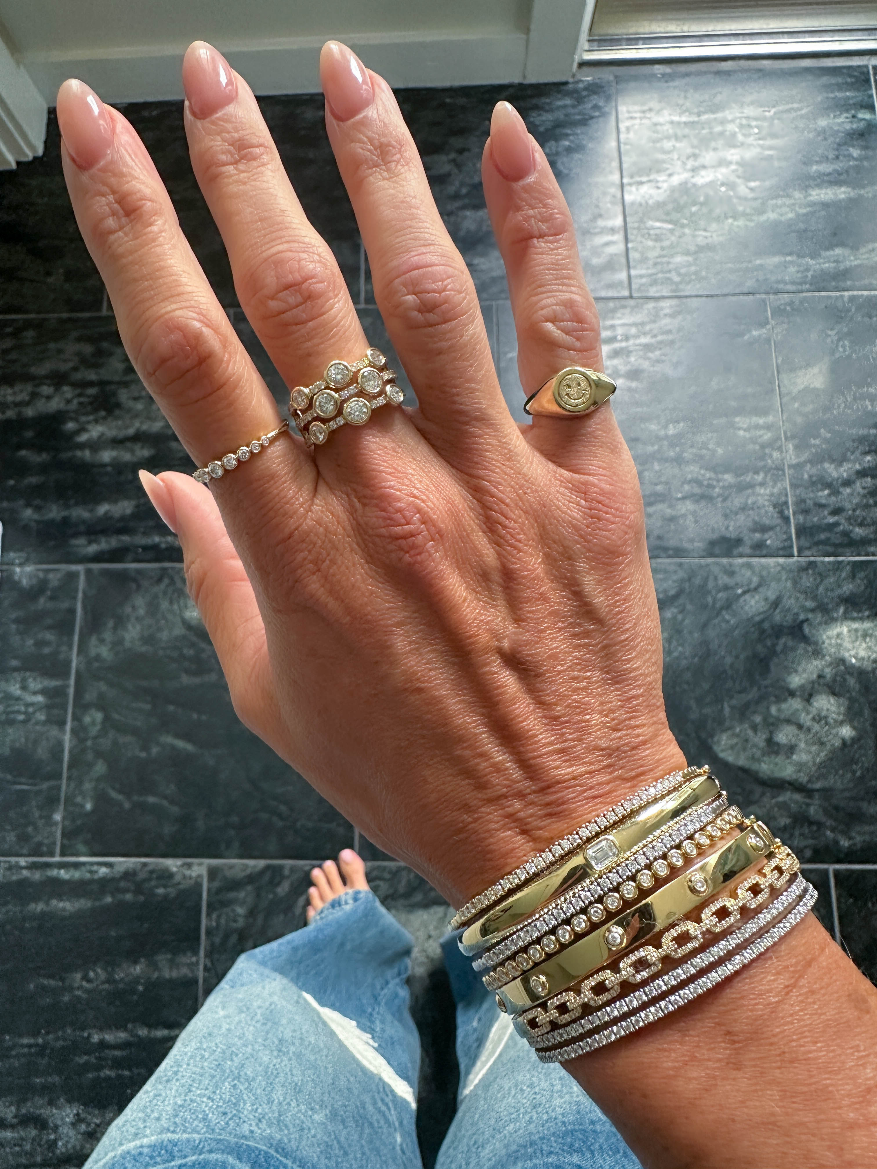 Hand with multiple rings and bracelets on a dark tiled floor