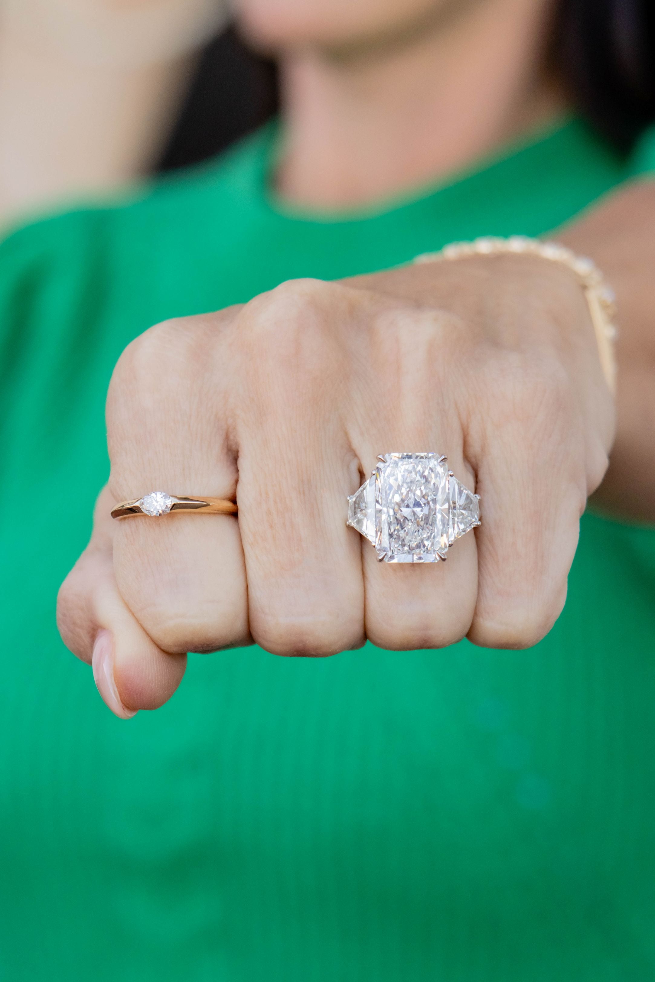 Close-up of a hand wearing two diamond rings with a green background
