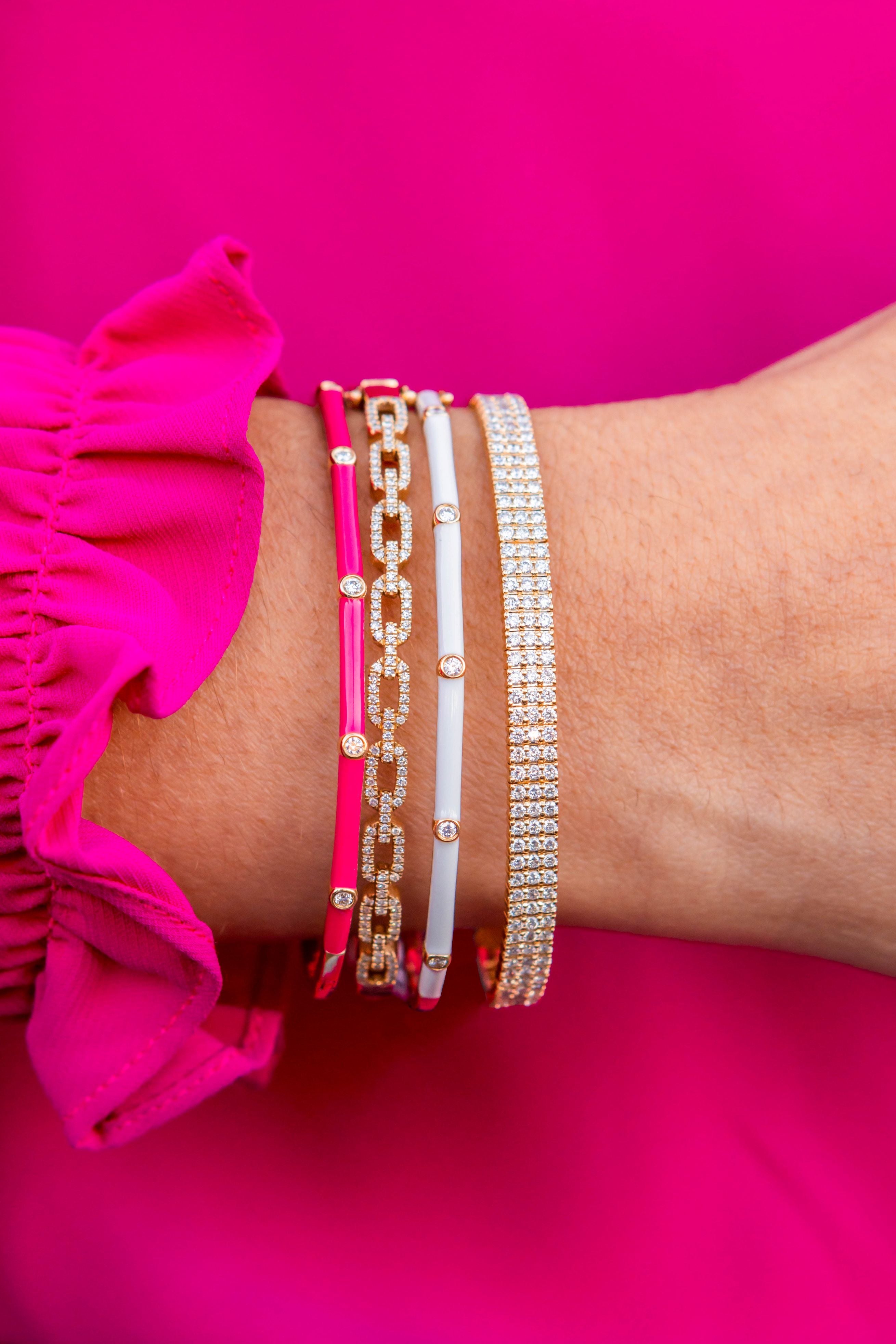 Close-up of a wrist wearing multiple bracelets on a bright pink background