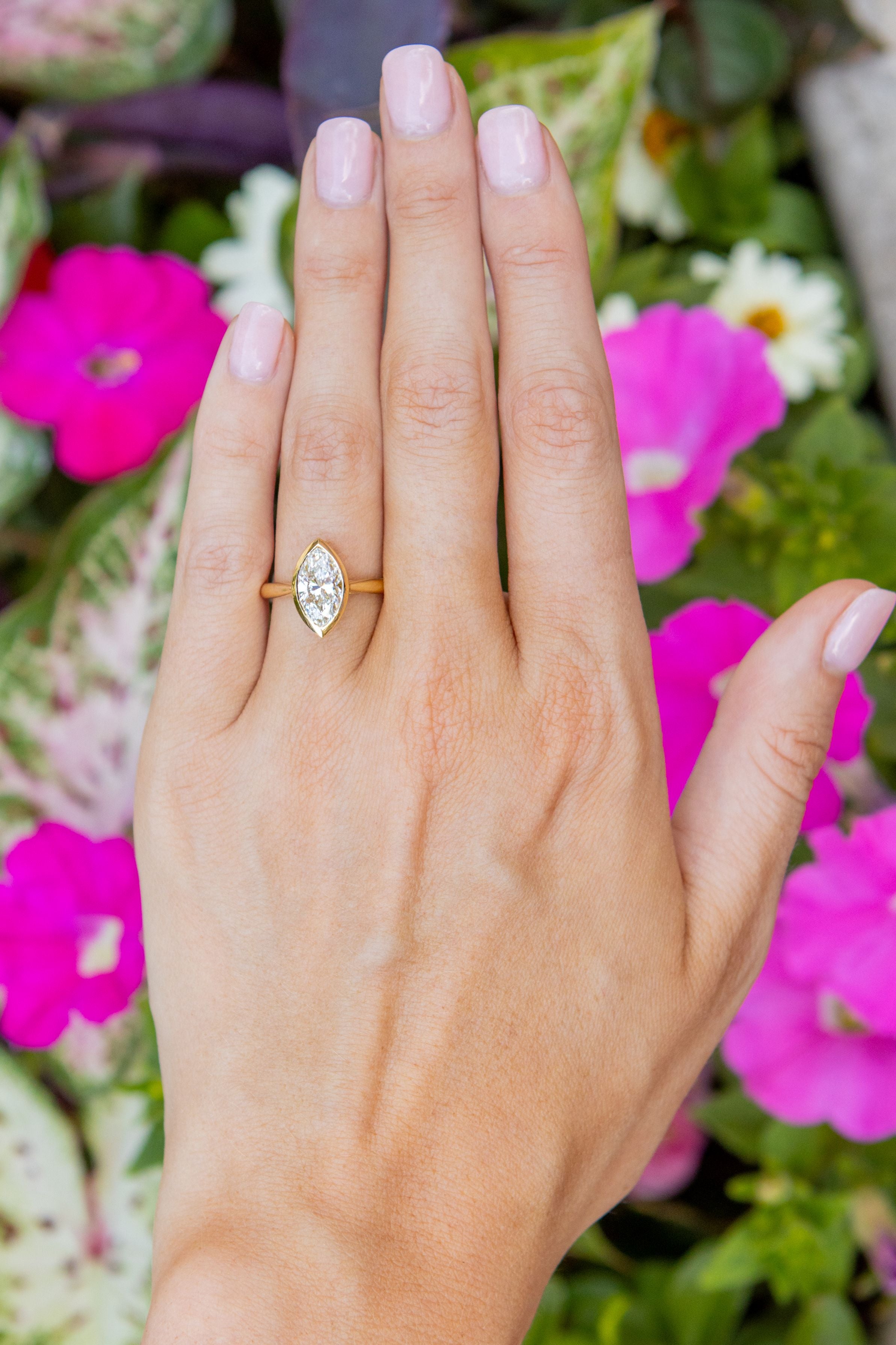 marquise diamond ring on a hand with pink flowers and green leaves in the background
