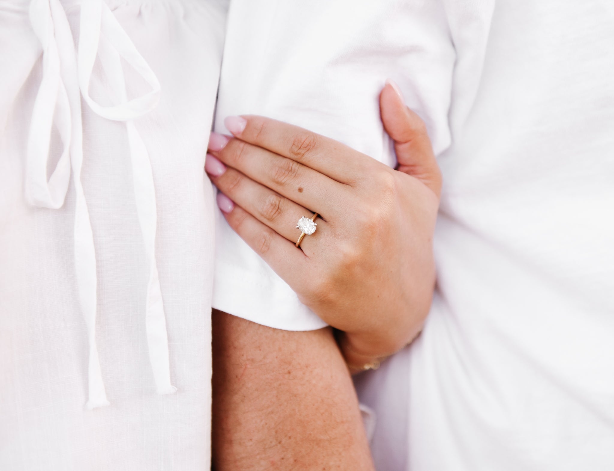 Close-up of a hand wearing a gold ring with a diamond, holding onto a white garment.
