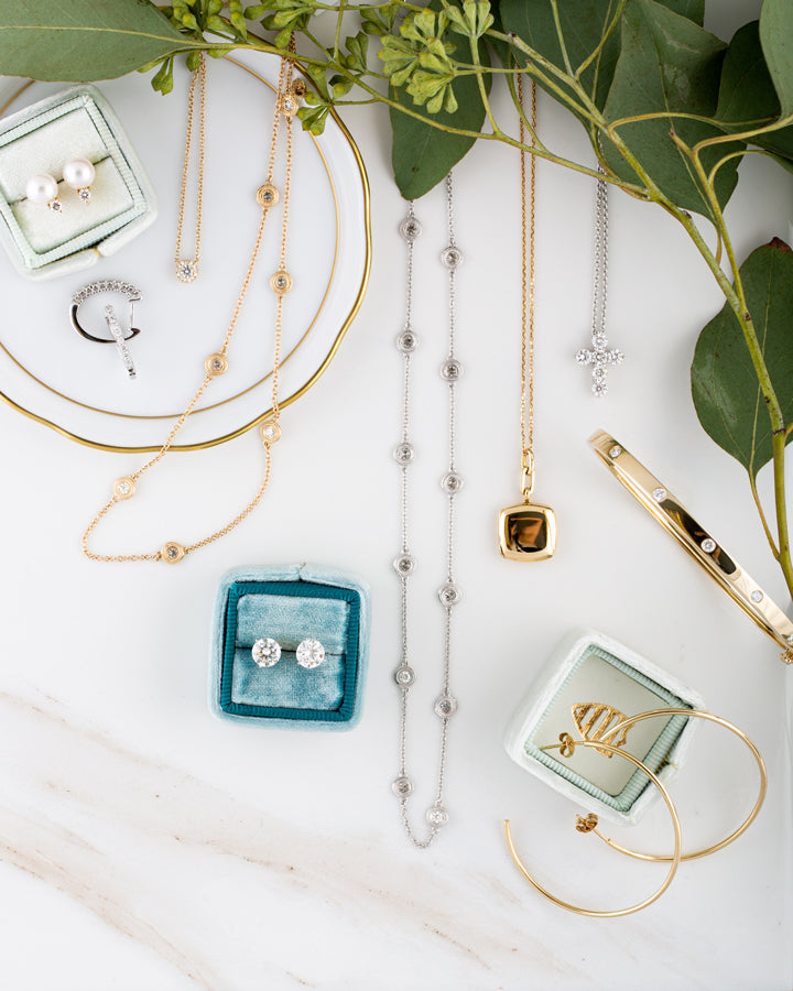 Jewelry including necklaces, earrings, and a bracelet on a white surface with green leaves.