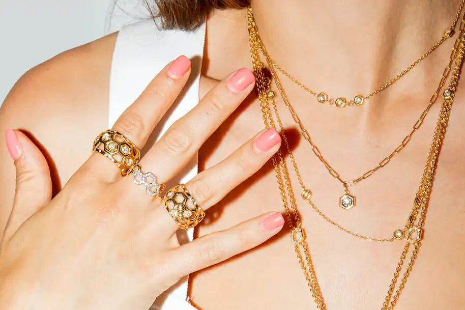 Close-up of a person wearing gold jewelry including necklaces, rings, and earrings on a light gray background.
