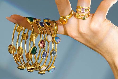 Gold jewelry with gemstones on a hand against a gradient background