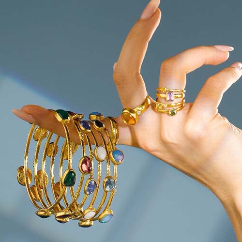 Gold jewelry with gemstones on a hand against a gradient background