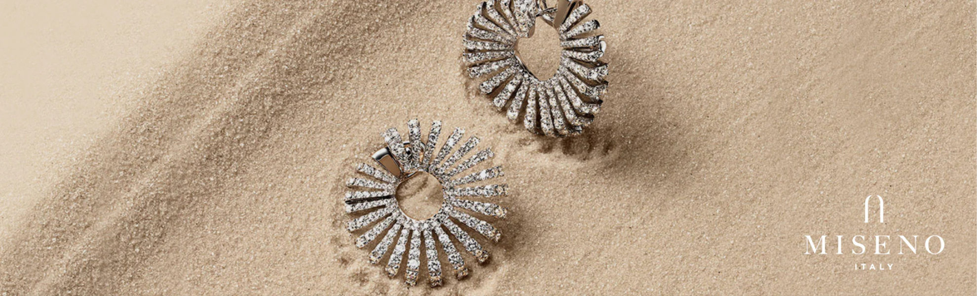 Pair of silver earrings on sand with Miseno logo