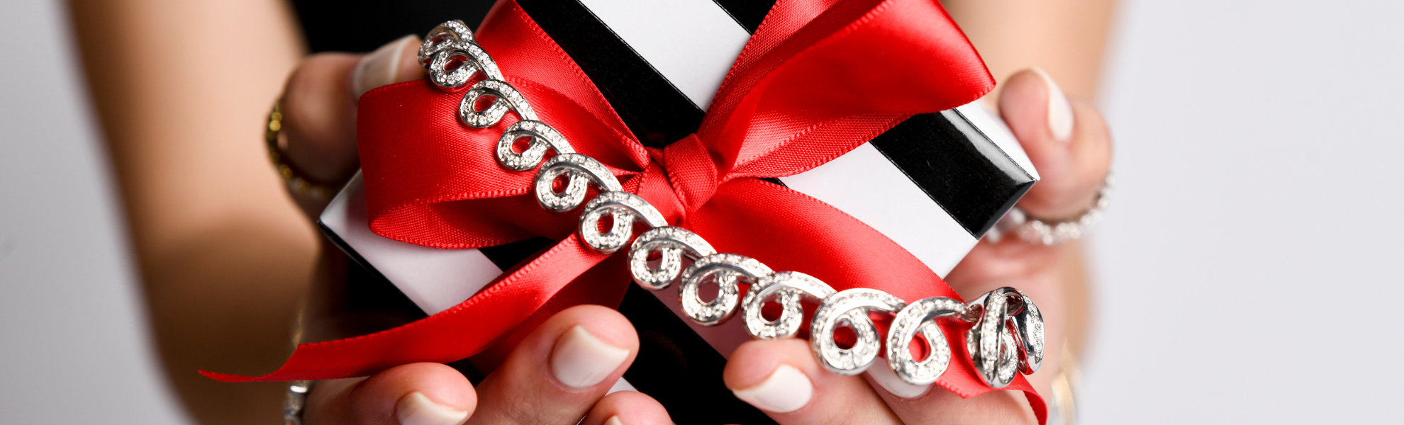 Silver bracelet with a red ribbon held by hands against a neutral background