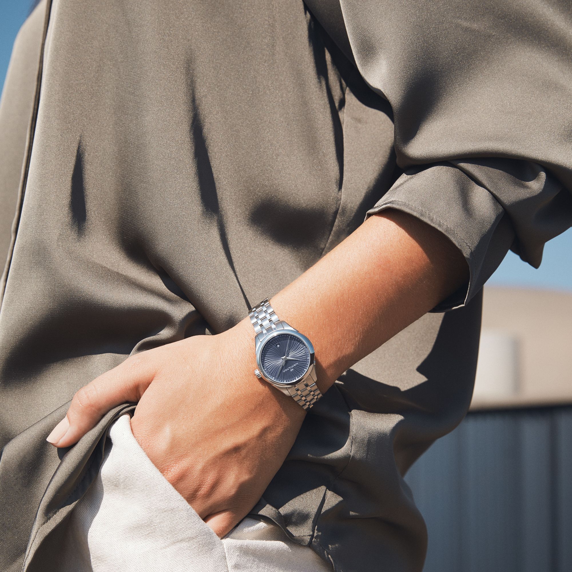 Person wearing a silver watch on a blurred outdoor background