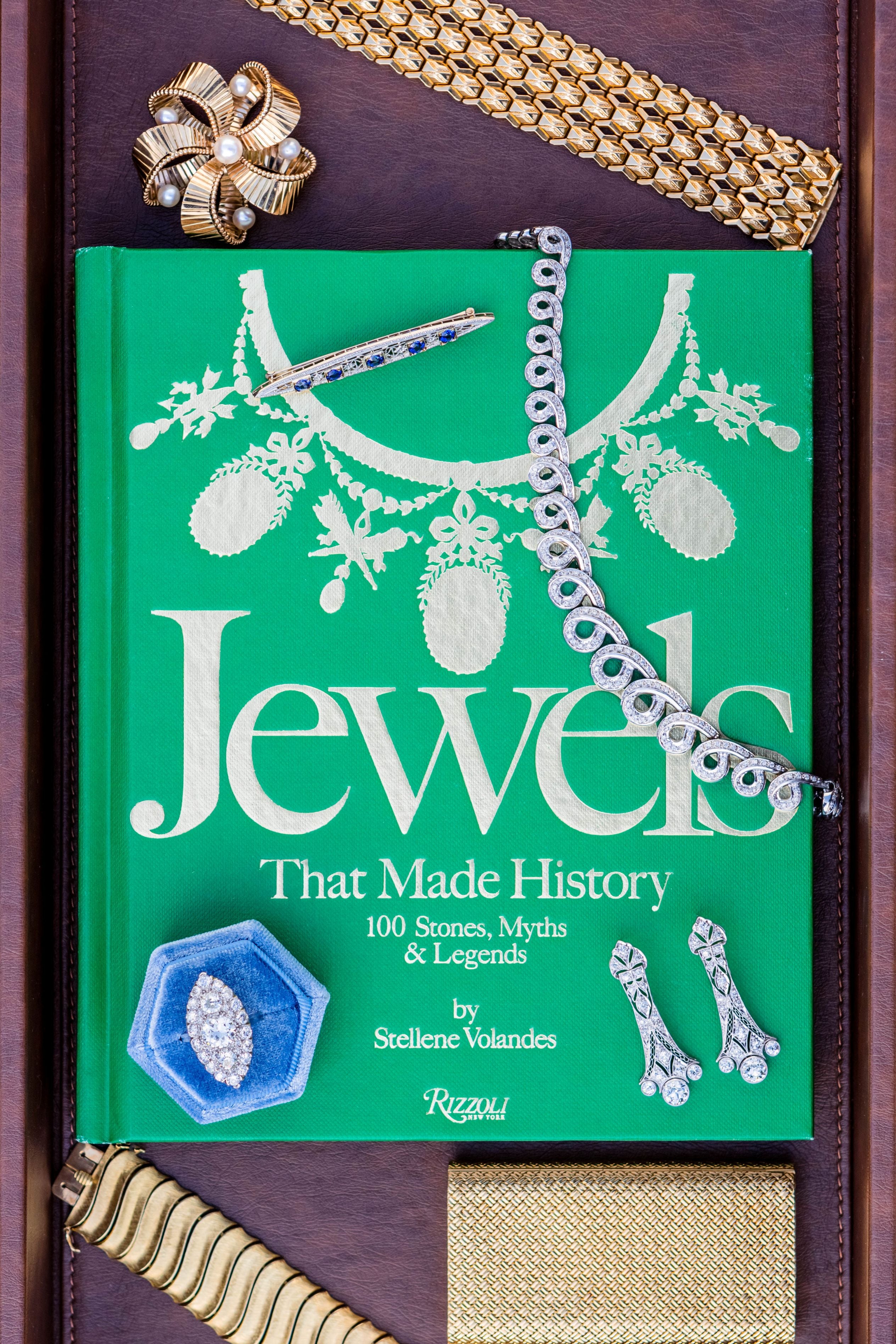 Book titled 'Jewels That Made History' with jewelry items on a wooden surface