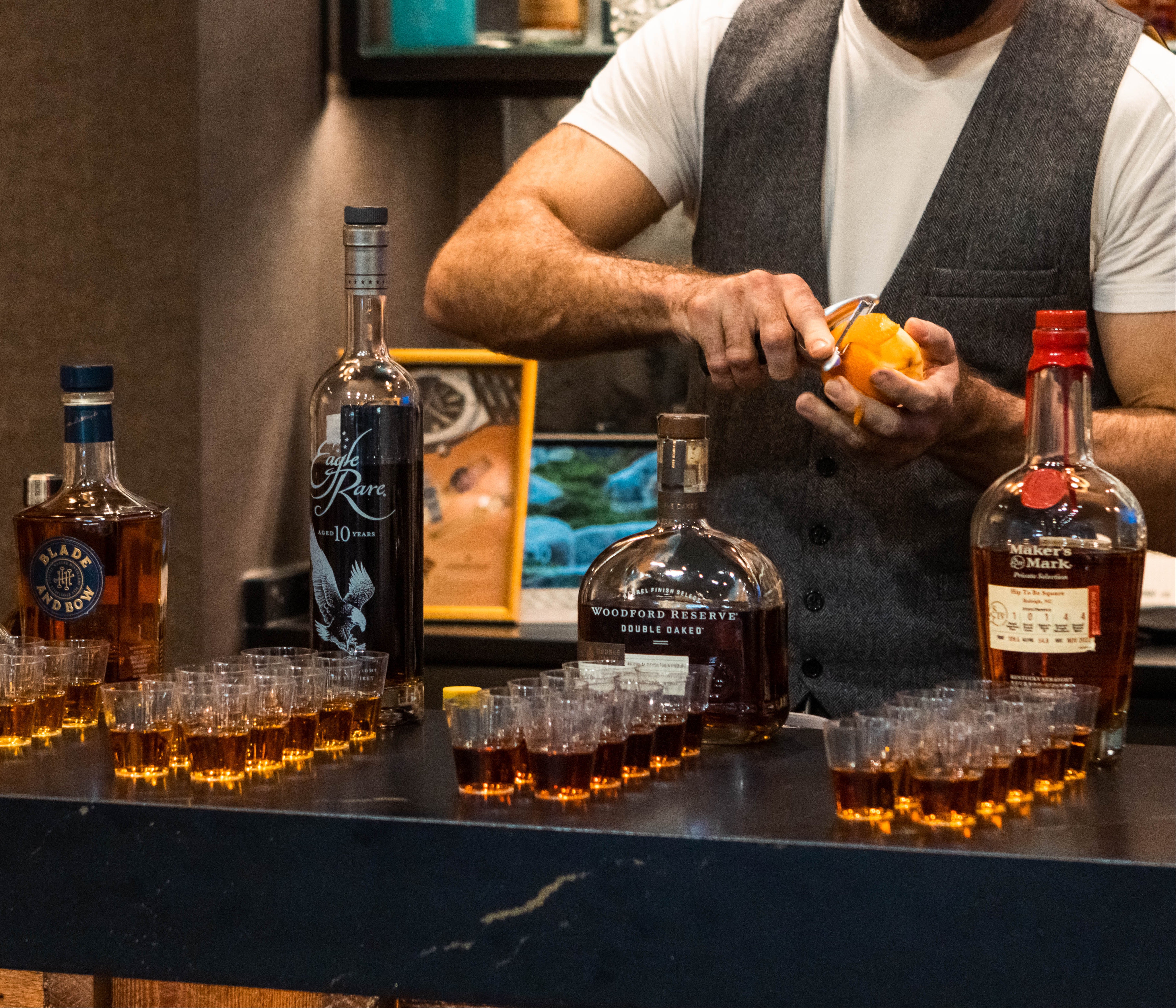 Bartender preparing drinks with whiskey bottles and glasses on a bar counter.