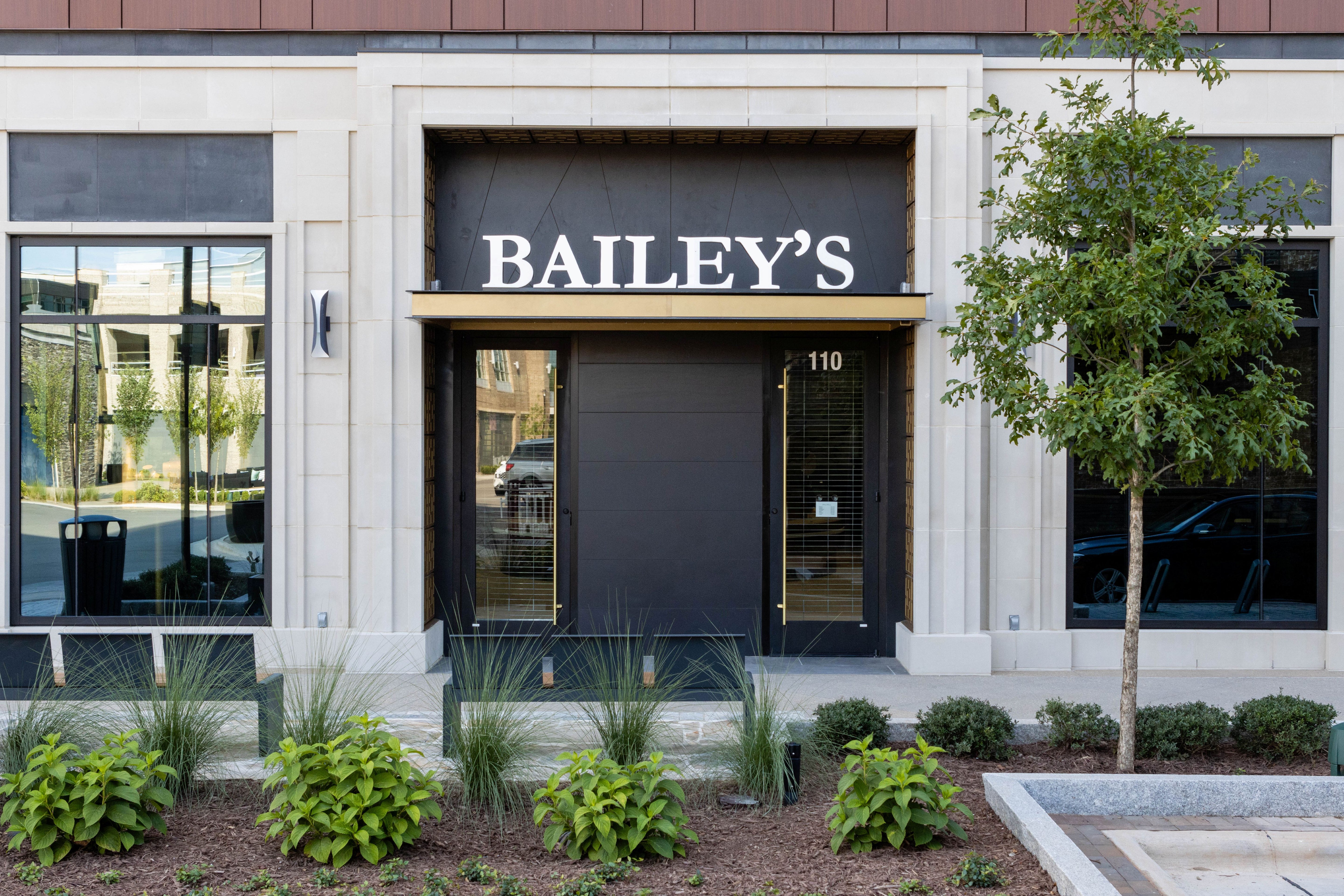 Bailey's store front with decorative plants and a tree.