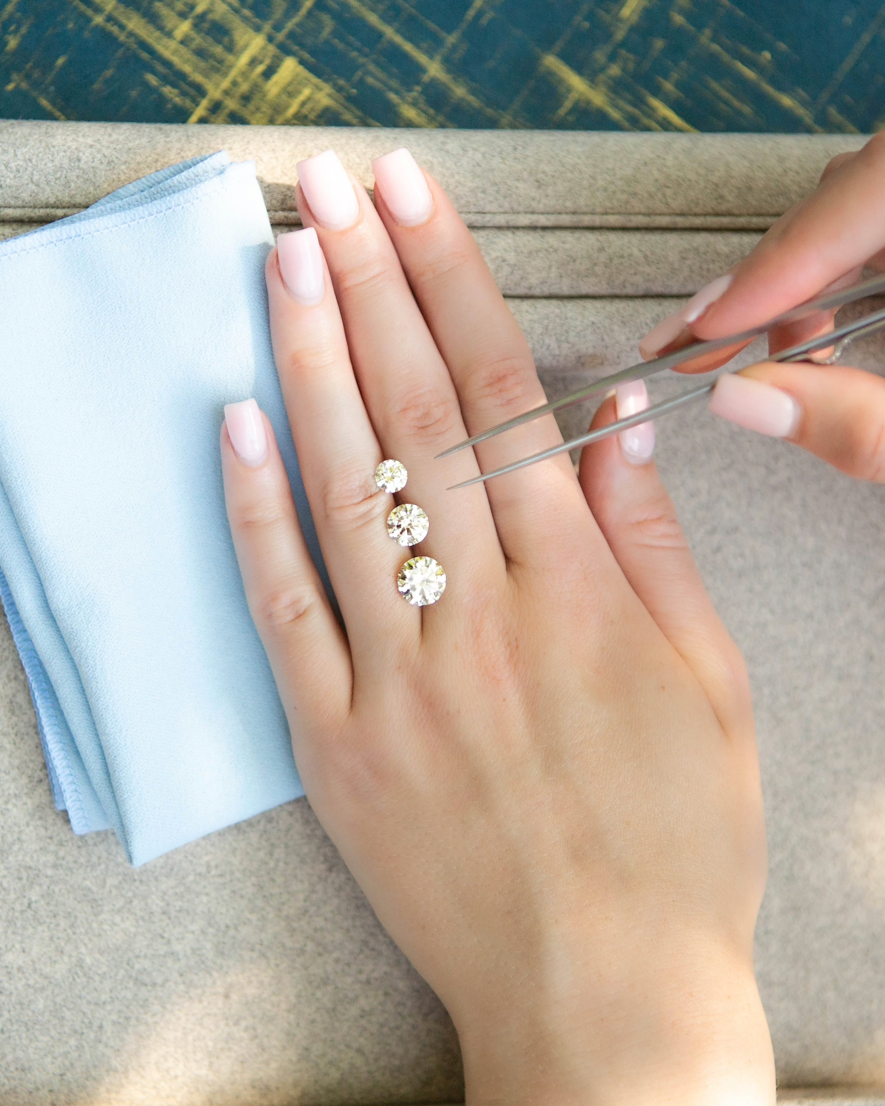 Close-up of a hand wearing a diamond ring with a blue cloth and beige surface in the background.