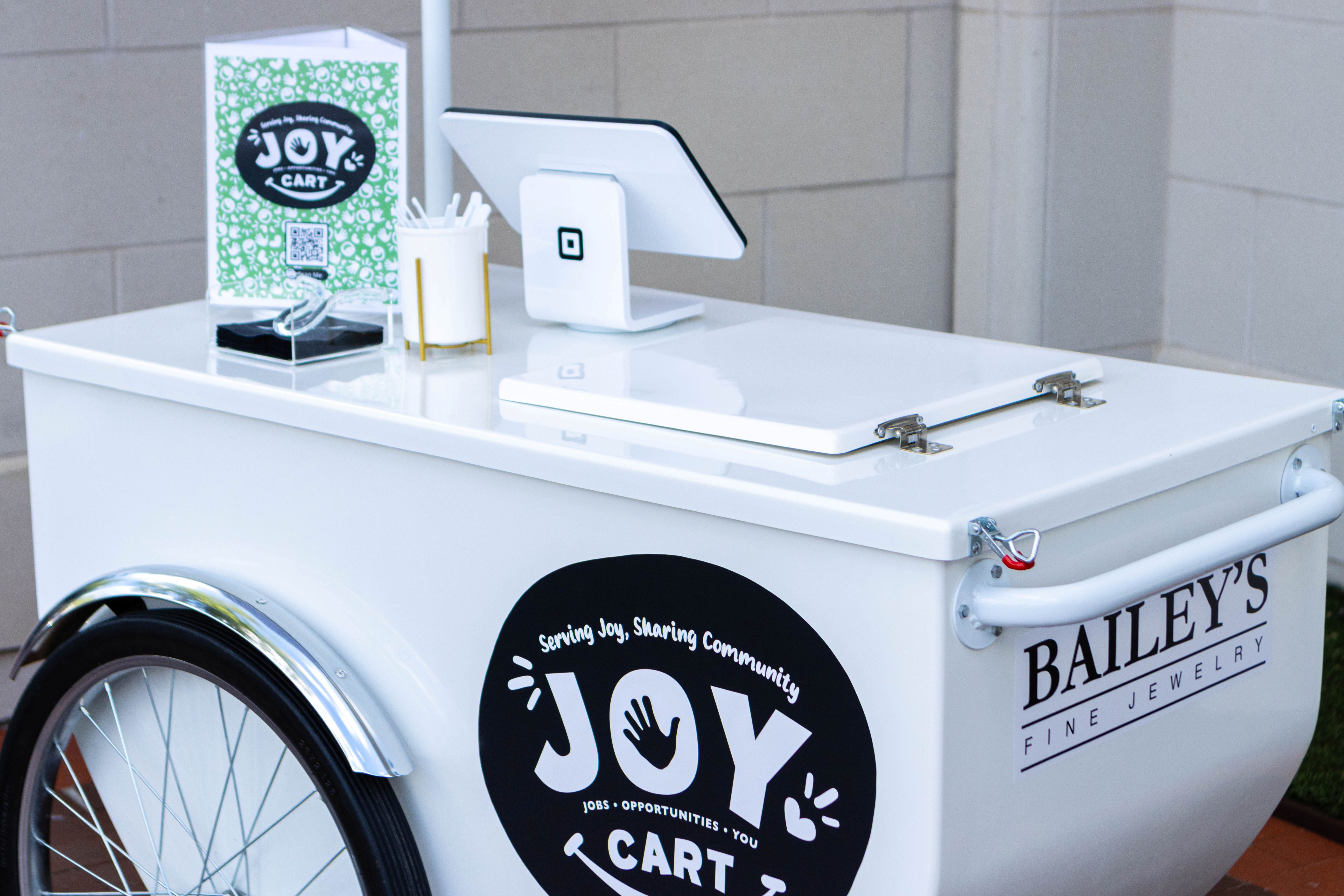 White 'Joy Cart' with branding and digital display on a tiled wall background