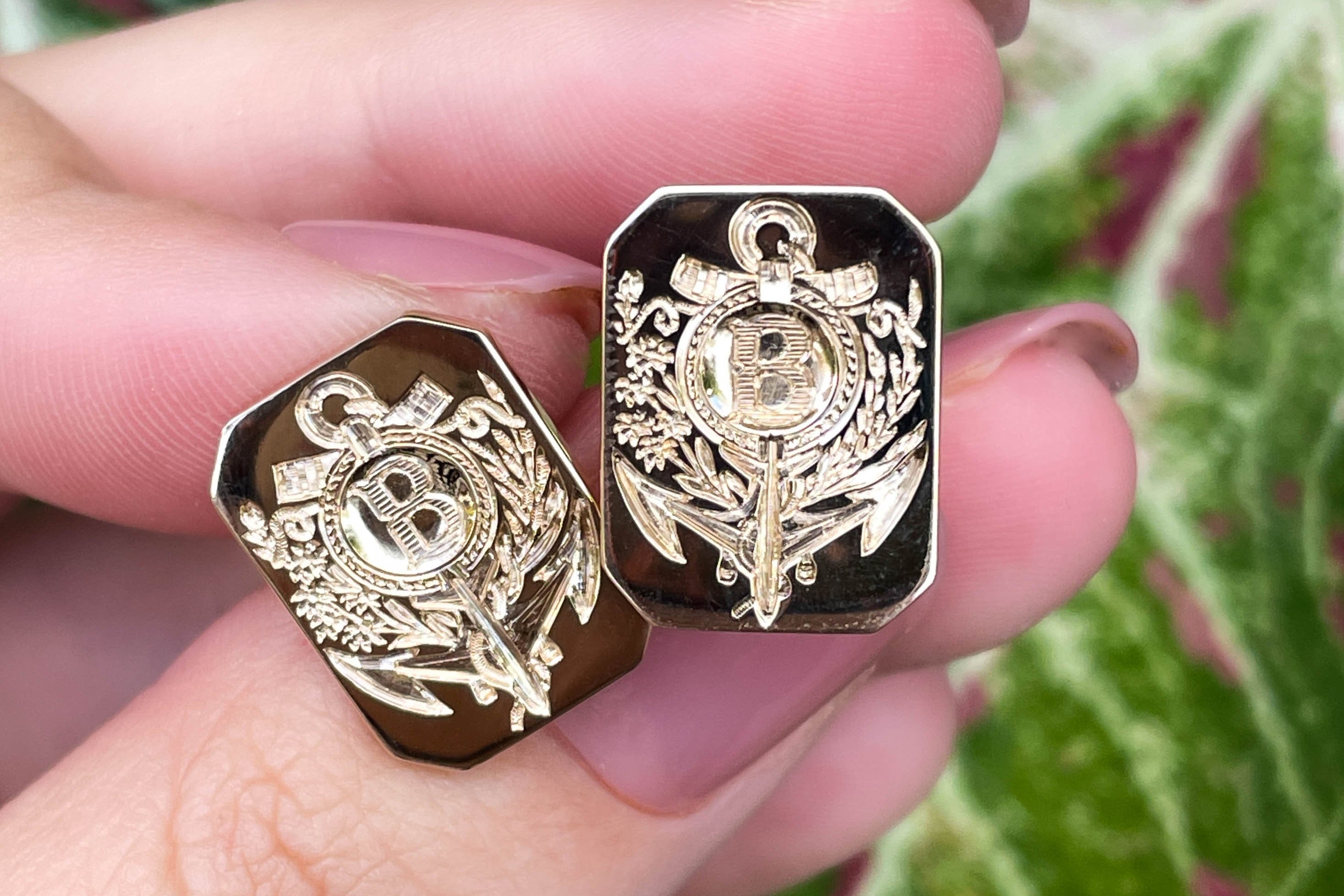 Gold decorative items held between fingers with a green leafy background
