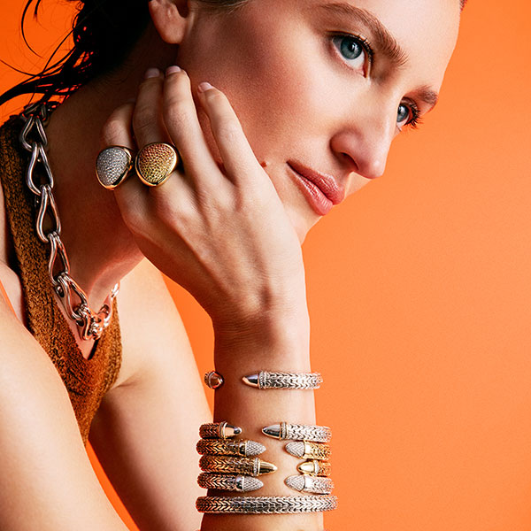 Woman wearing multiple pieces of jewelry including rings and bracelets on an orange background