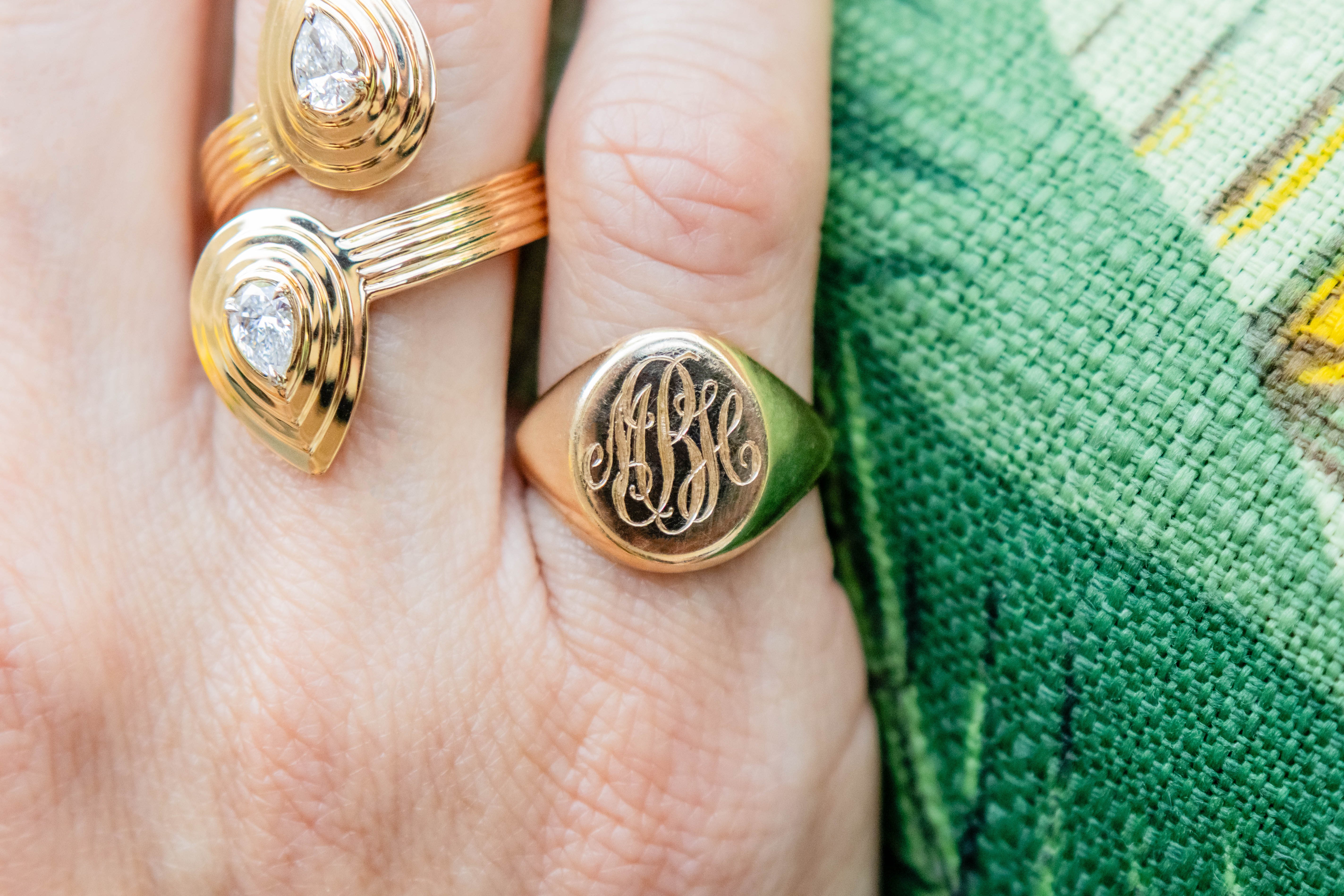 Gold rings with engraved designs on a hand against a green fabric background