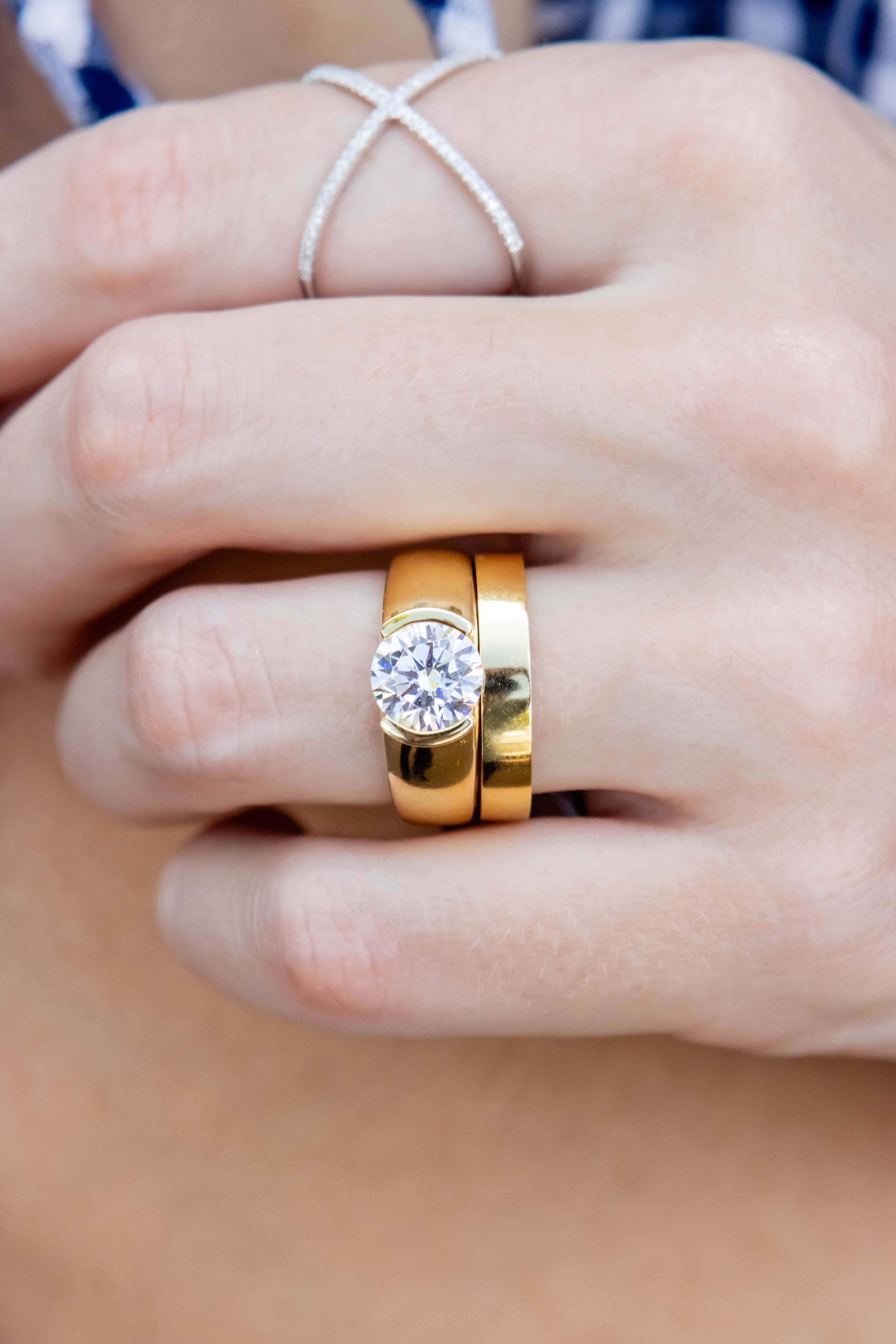 hand wearing diamond and gold rings on a blurred neutral background