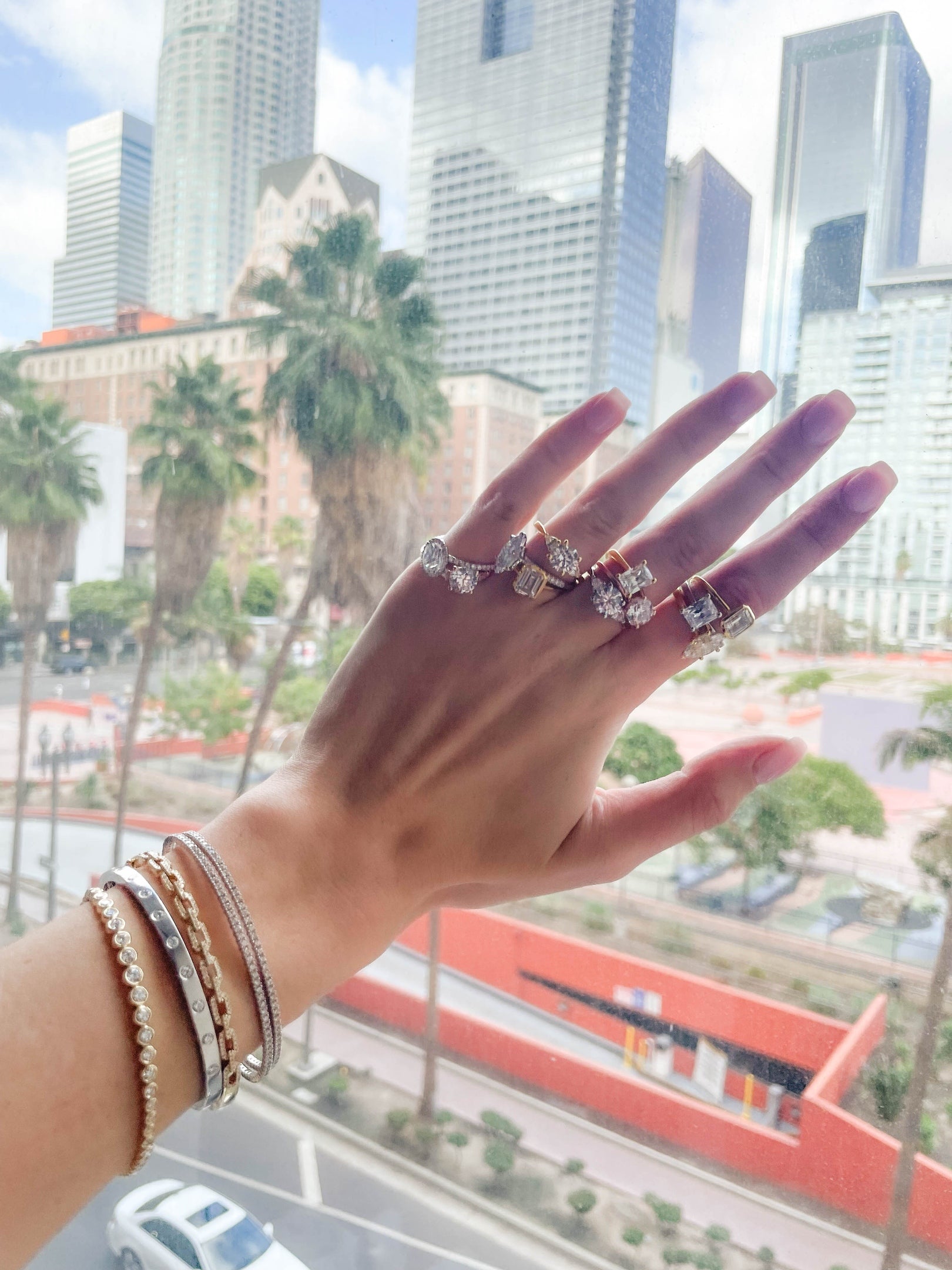 Hand wearing multiple diamond rings with a cityscape in the background