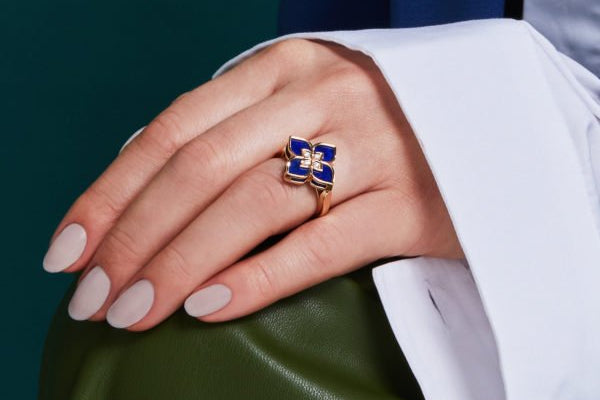 Hand wearing a blue and gold ring with a green background
