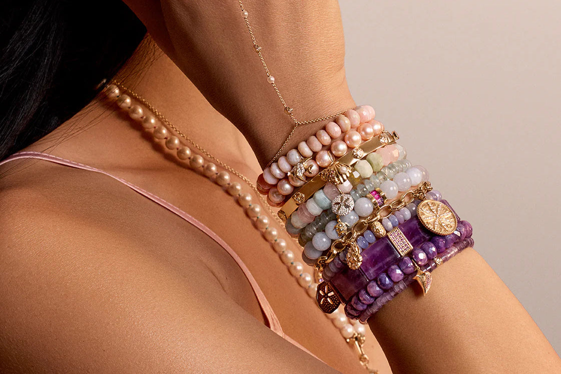 Woman wearing multiple bracelets and a necklace with a neutral background