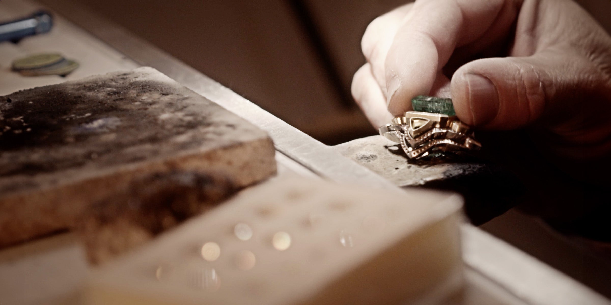 Close-up of a jeweler working on a gold ring with a green gemstone.