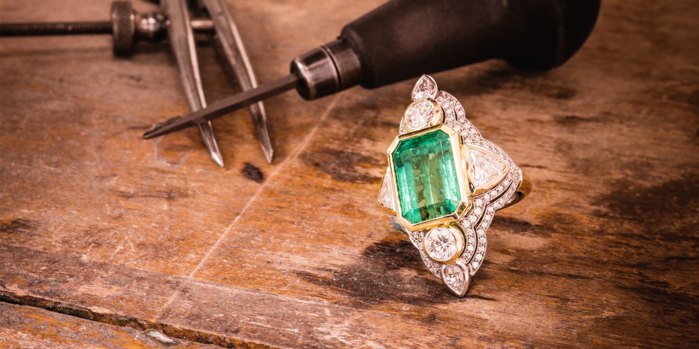 Emerald ring with diamond accents on a wooden surface with tools.