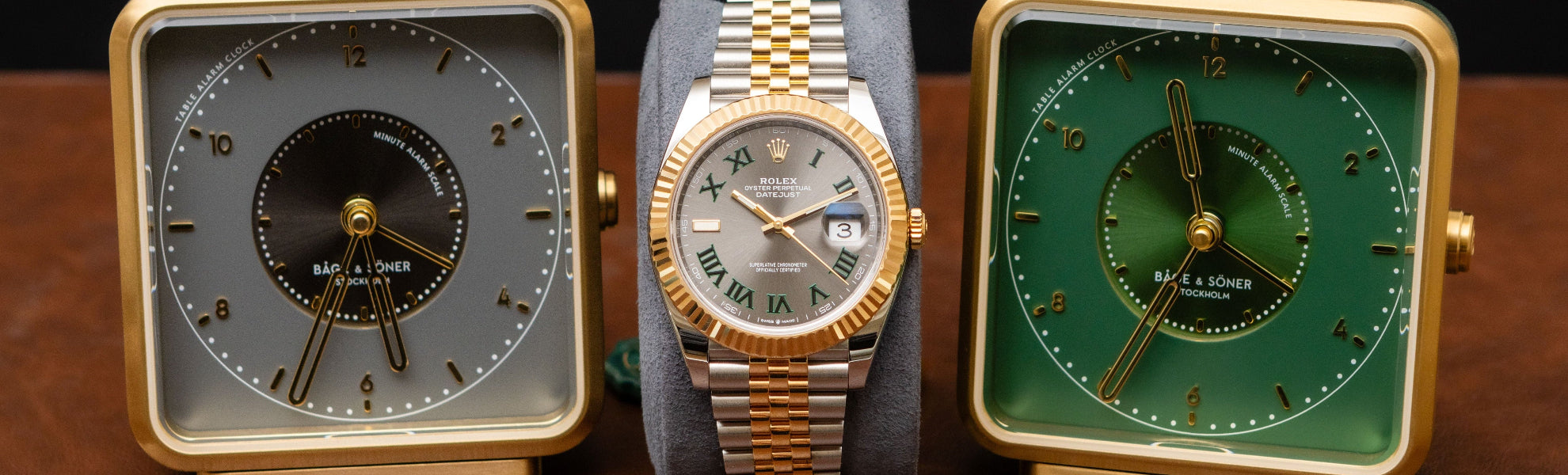 Rolex watch between two square clocks on wooden surface