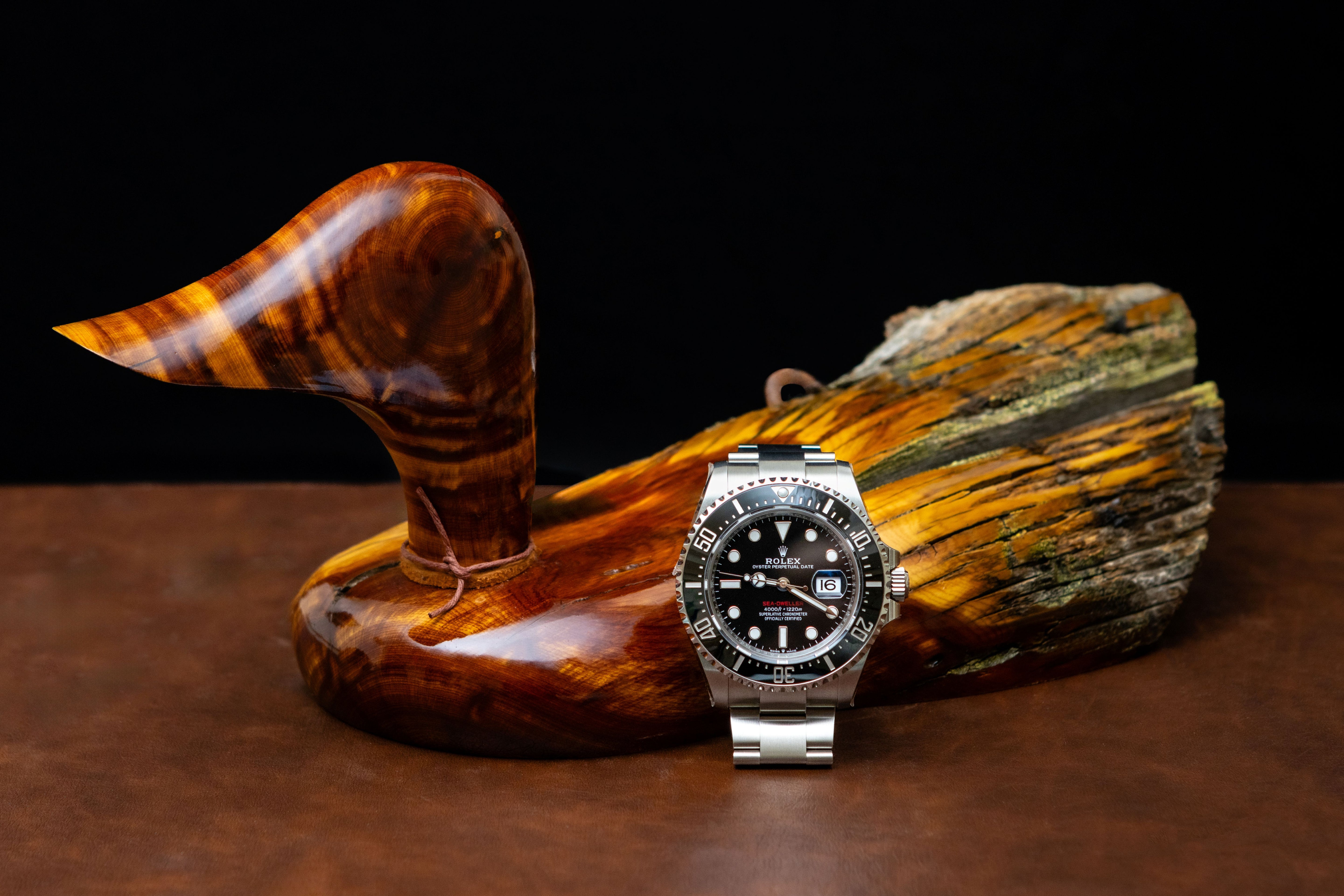 Silver watch with a black face on a wooden surface with carved wooden duck
