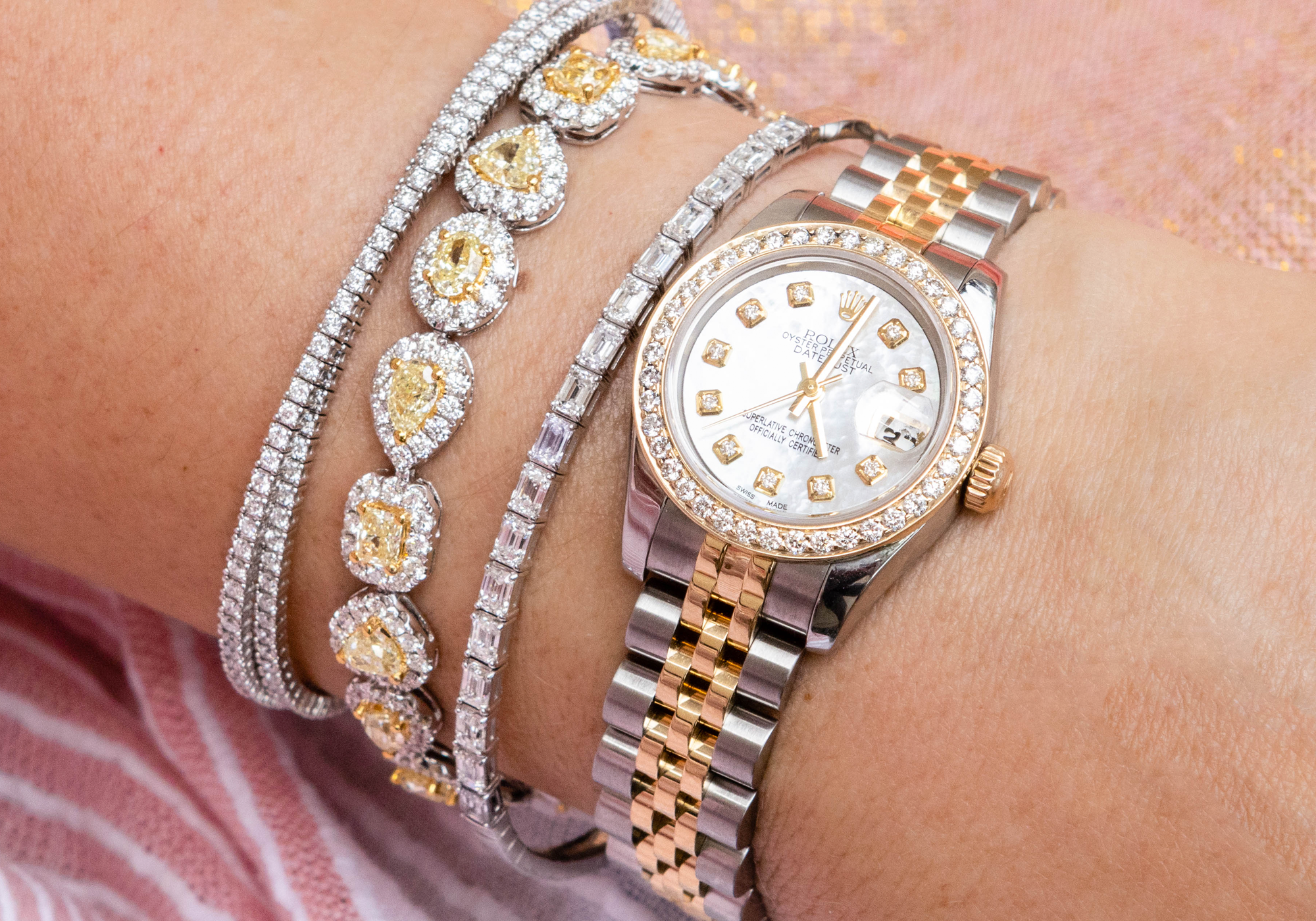 Gold and silver watch with diamond-studded bracelet on a wrist against a pink background
