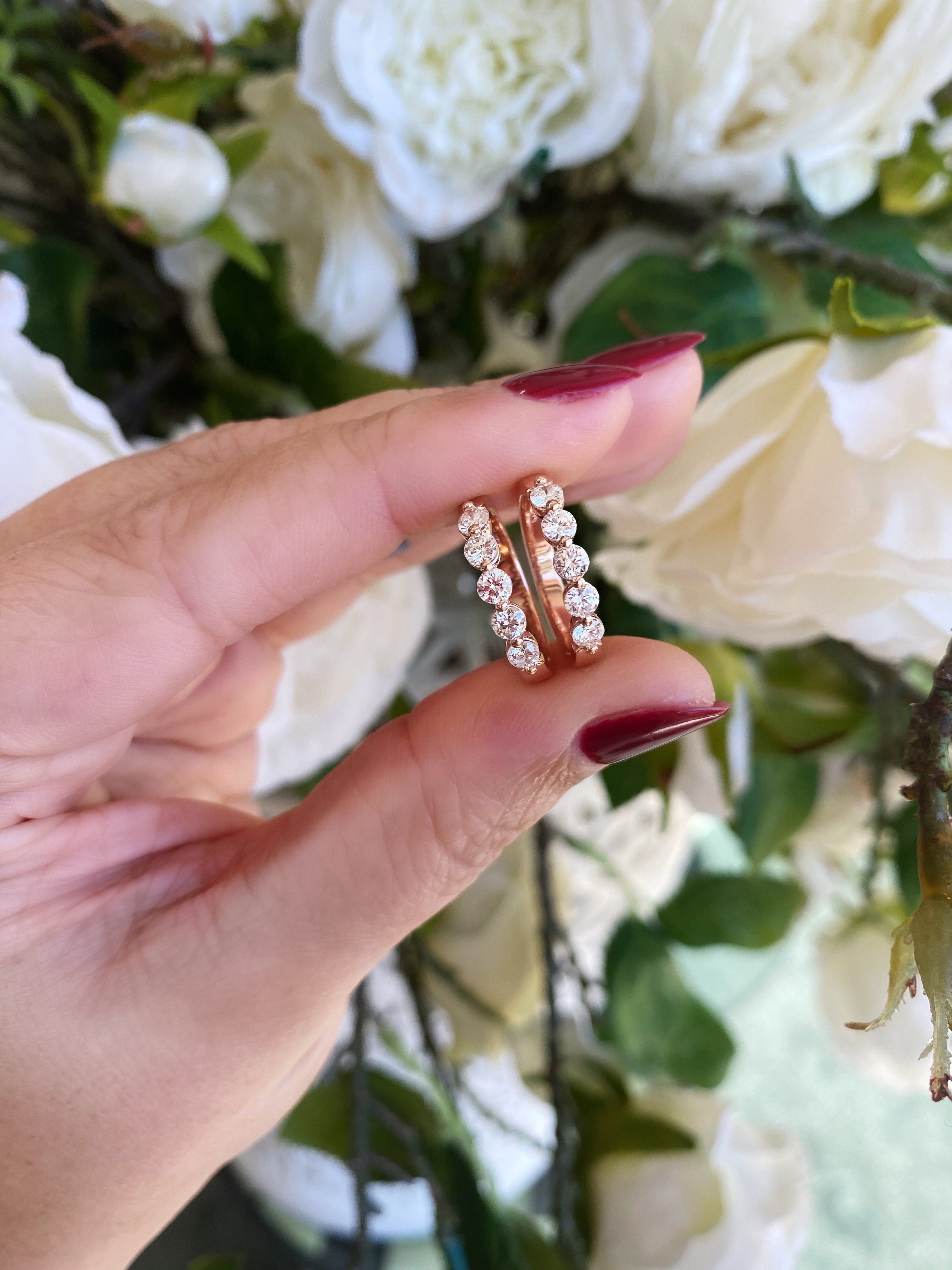Hand holding two gold rings with small diamonds against a floral background