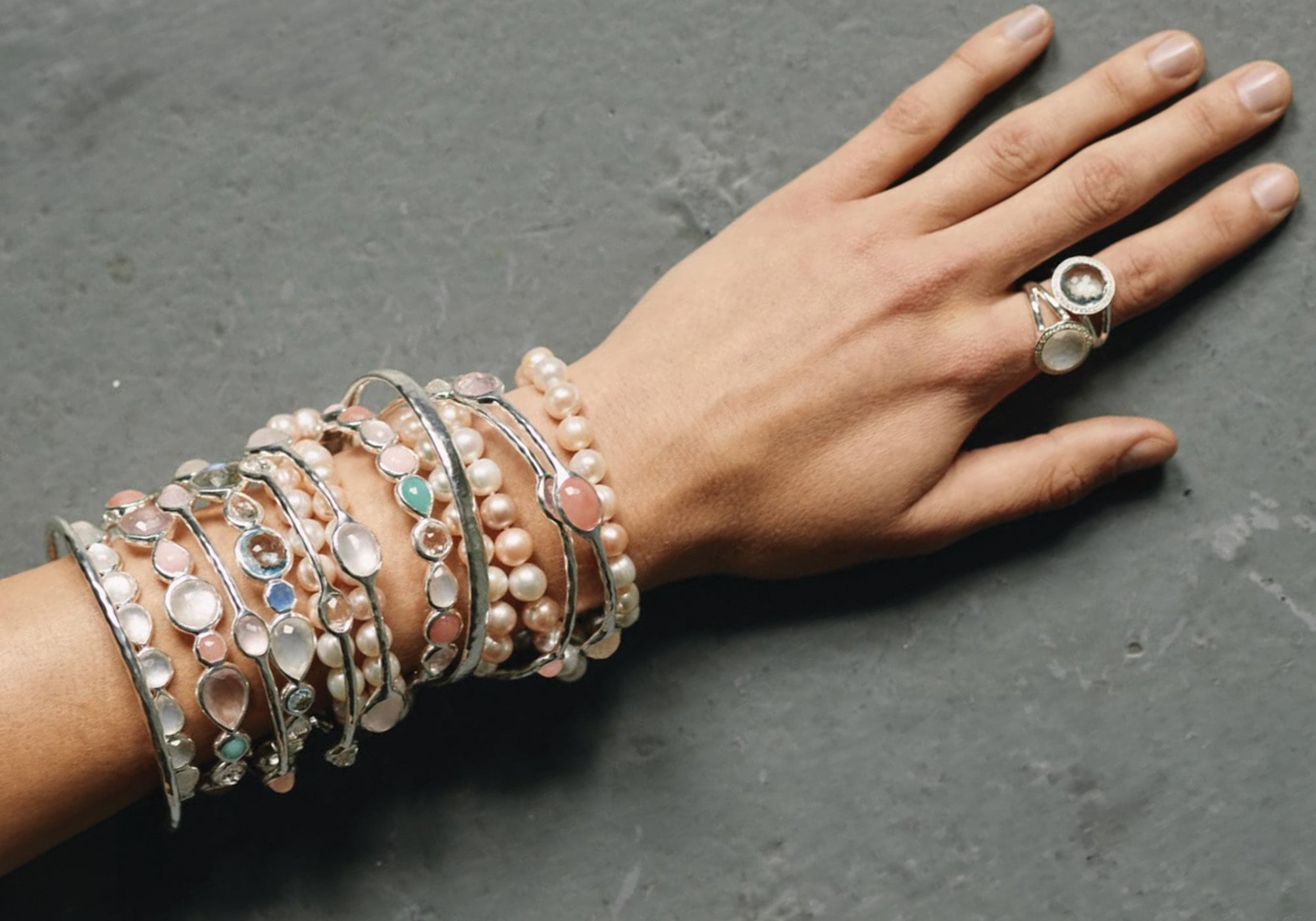 Hand wearing multiple bracelets and a ring on a dark surface