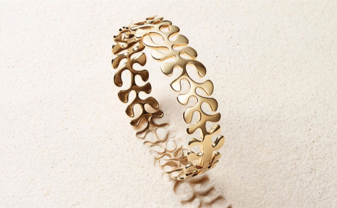 Gold bracelet with intricate design on a light beige sand background